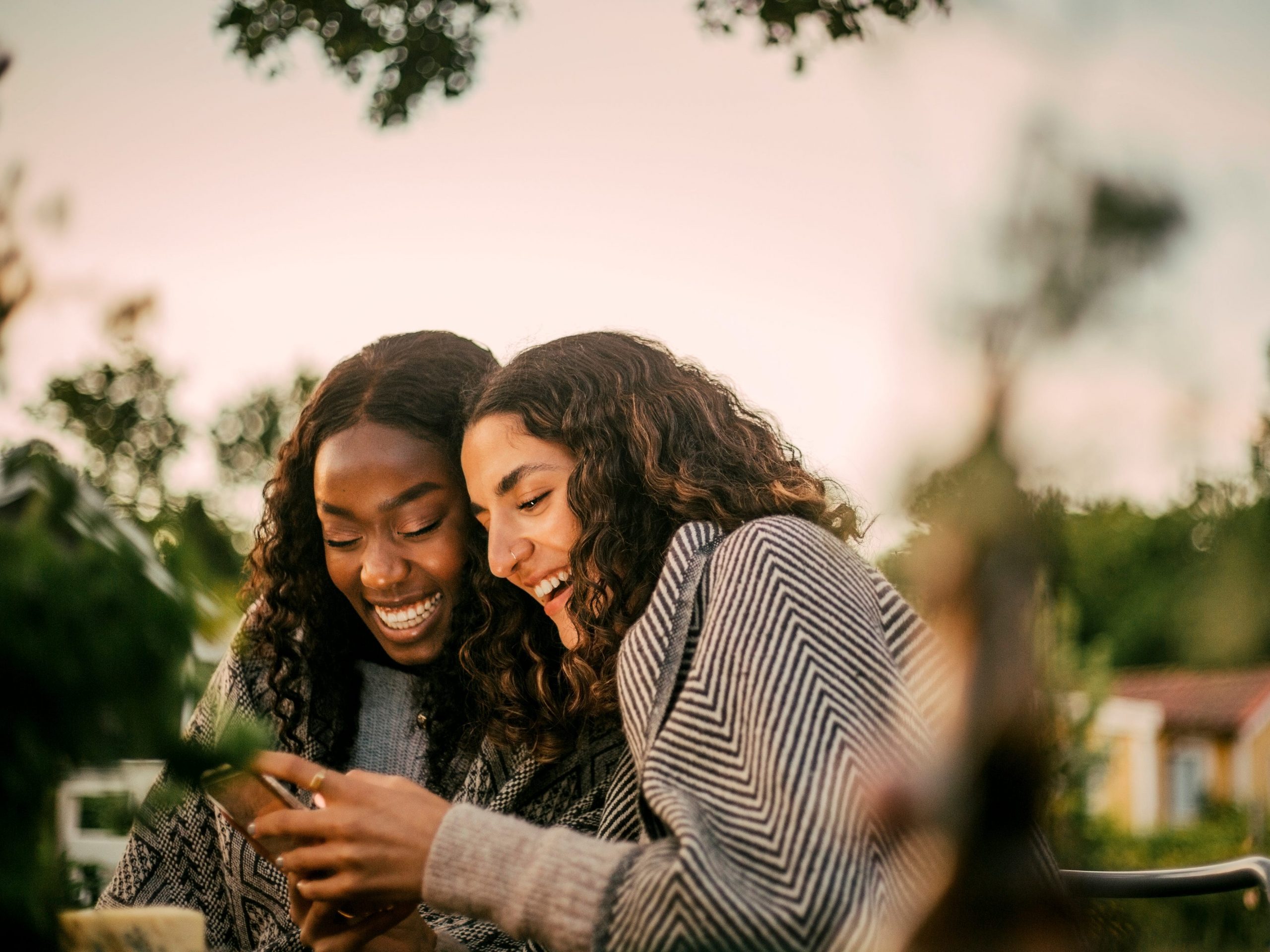 Cheerful friends using phone in backyard during social gathering