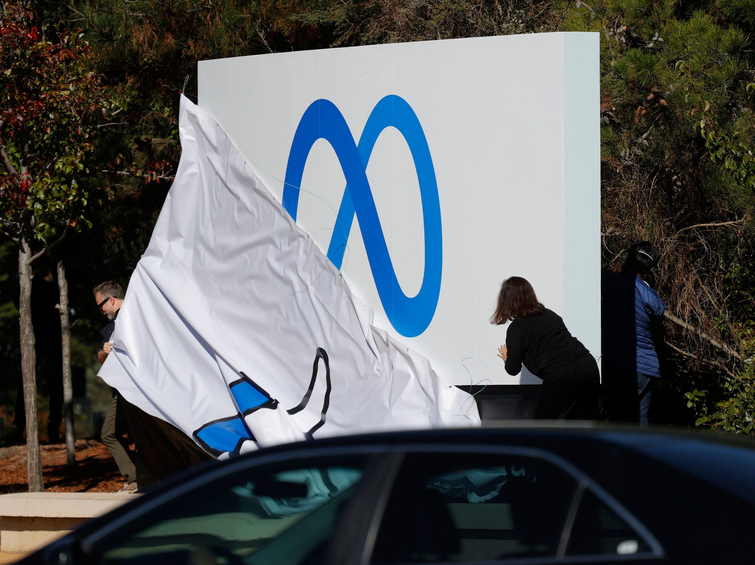 Workers in front of Facebook headquarters pull off cover of the old "thumbs up" sign to reveal the new Meta logo