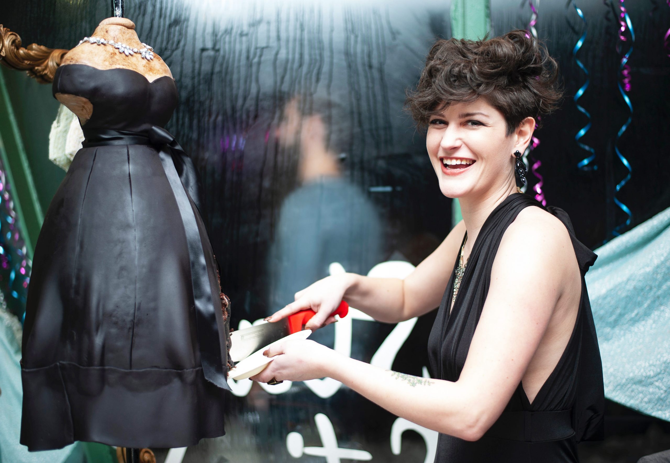 Justine Martin, who owns Guilty Pleasures Bakeshop, standing next to a large cake of a mannequin in a black dress.