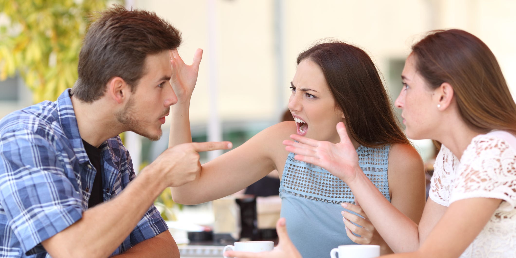 Two women and a man have a heated argument at a table.