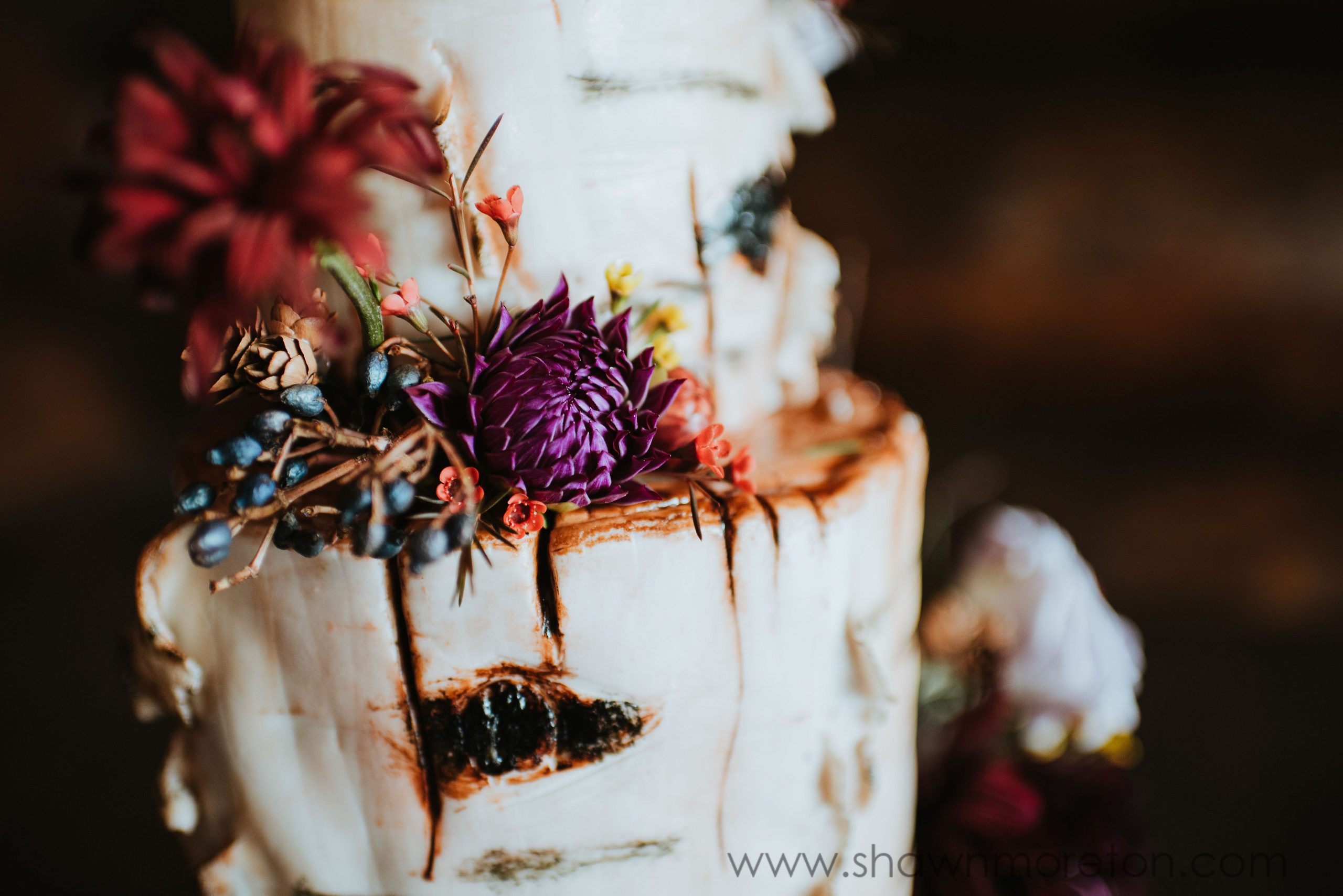 An off-white cake decorated with red and purple flowers.
