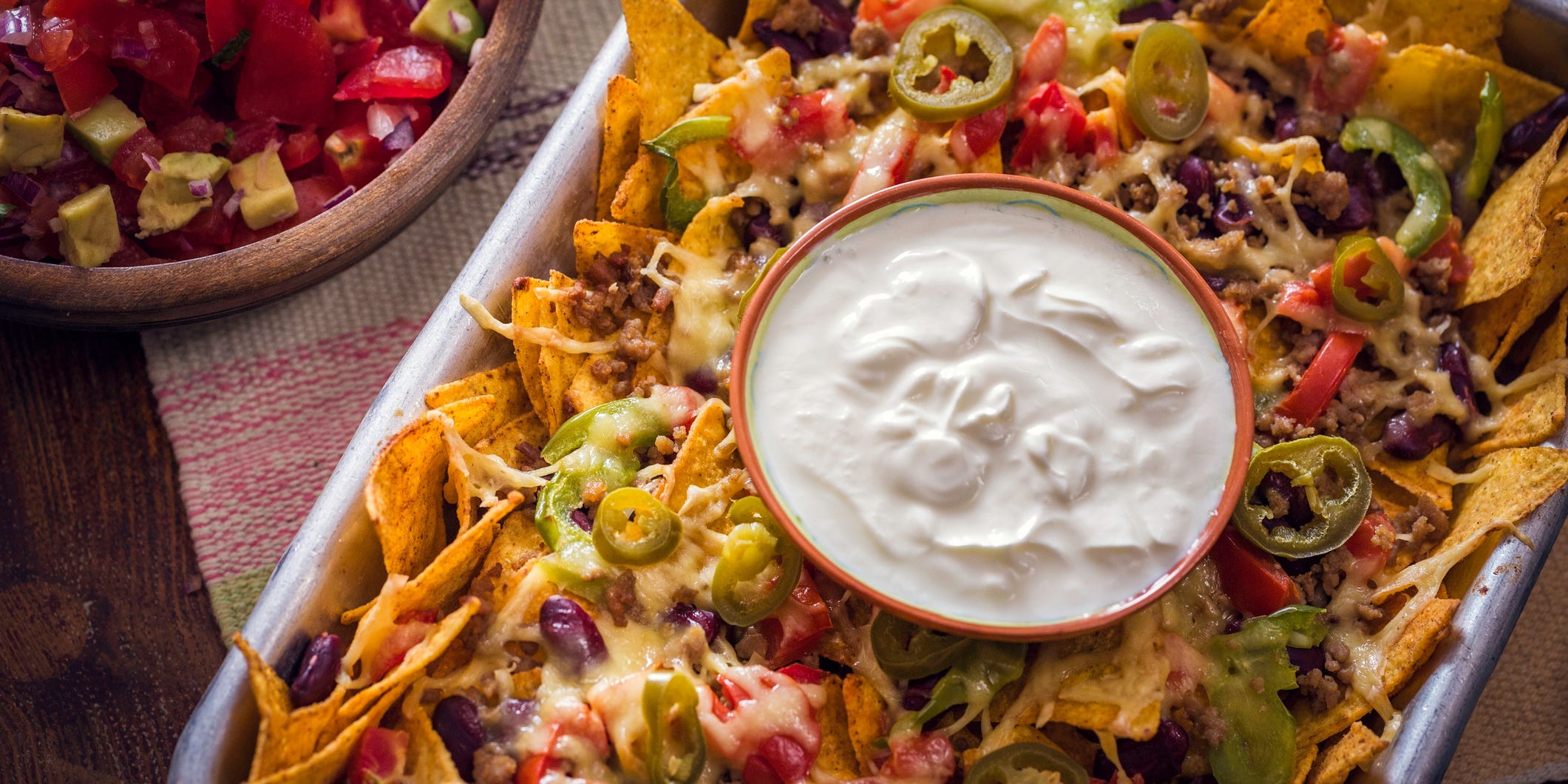 A sheet tray of nachos with a bowl of sour cream nestled into the center