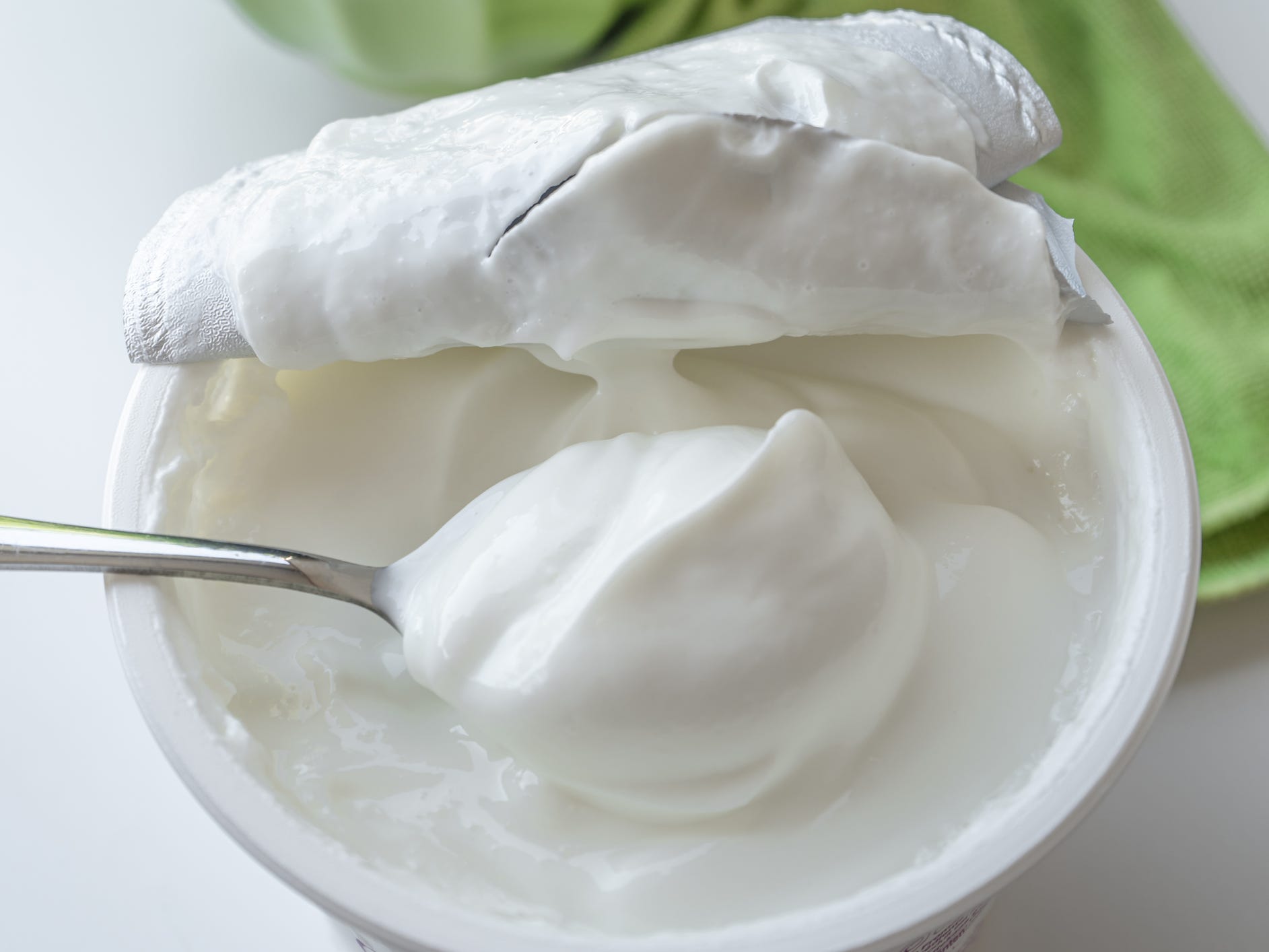 A container of sour cream with the lid pulled back and a spoon in it