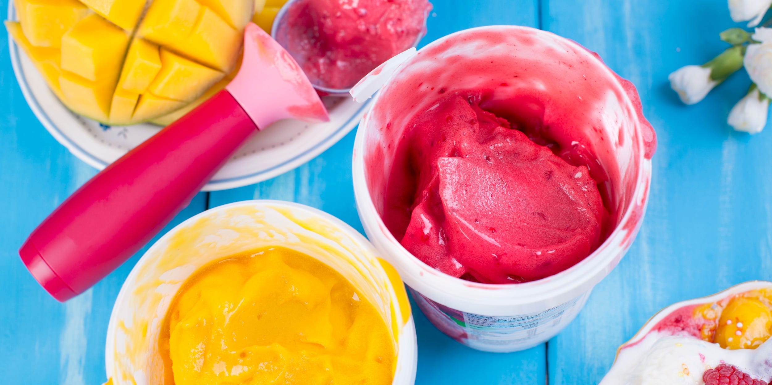 Two open pints of sorbet, one yellow and one pink, sit on a blue table.
