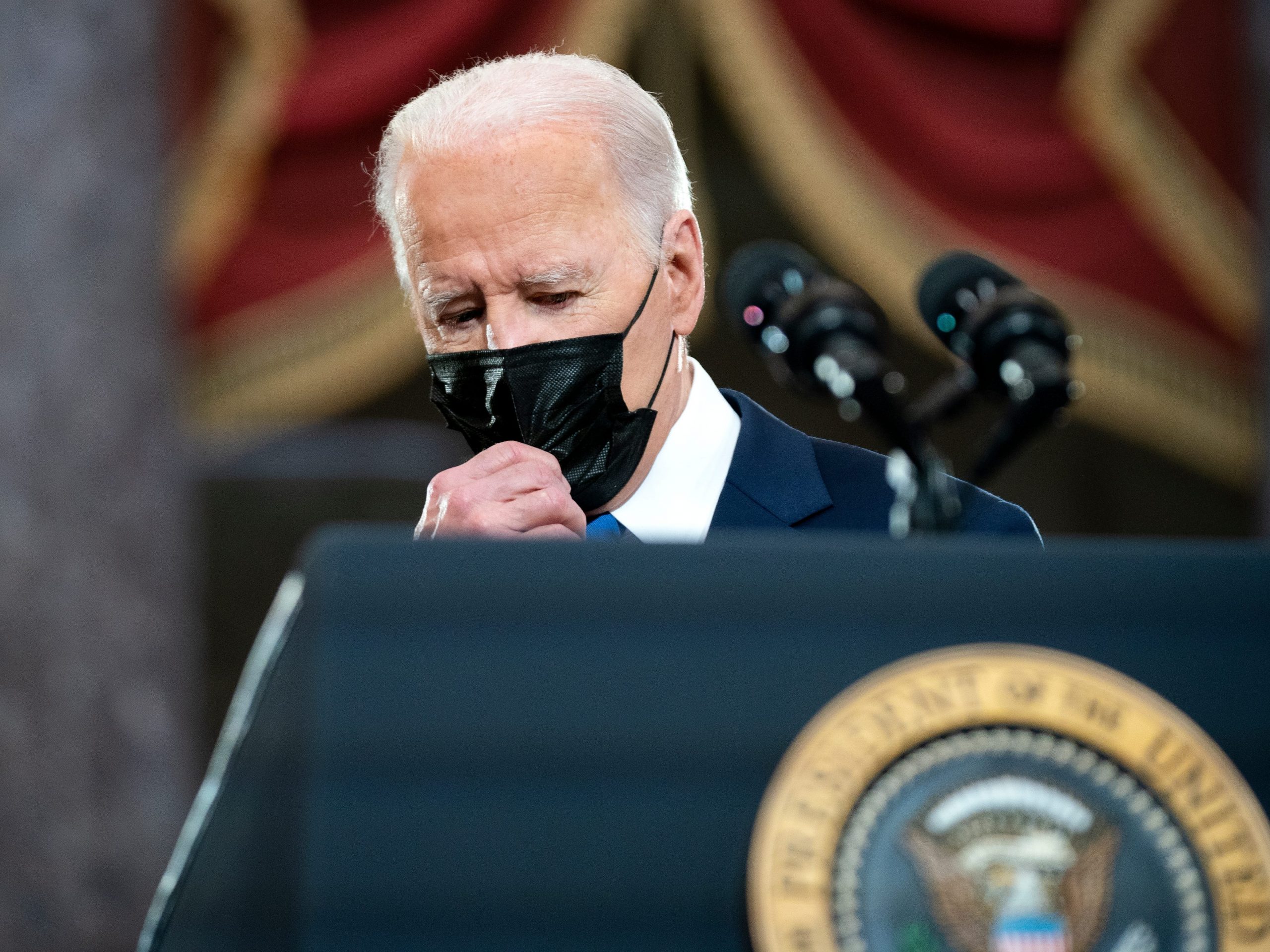 US President Joe Biden adjusts his mask as he stands on a podium