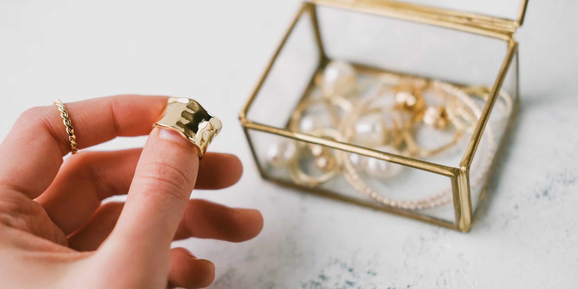 Person holding a gold ring with a jewelry box filled with gold jewelry in the background out of focus