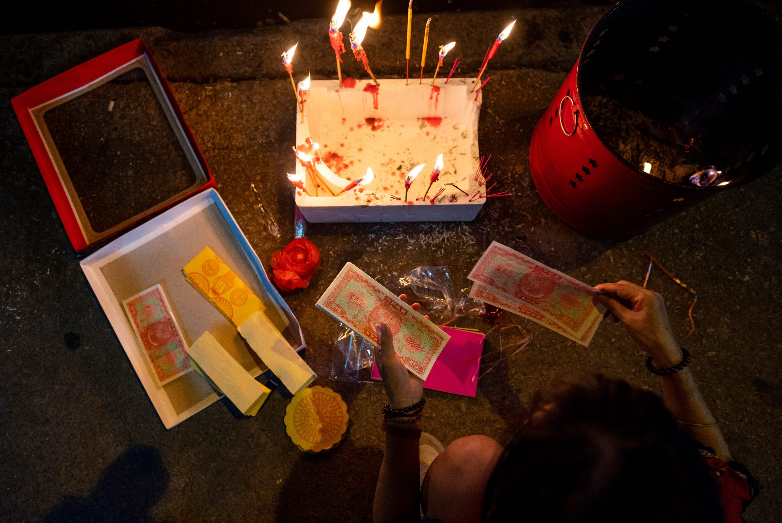 An overhead view of a Hong Kong resident preparing hell money and burning joss sticks.