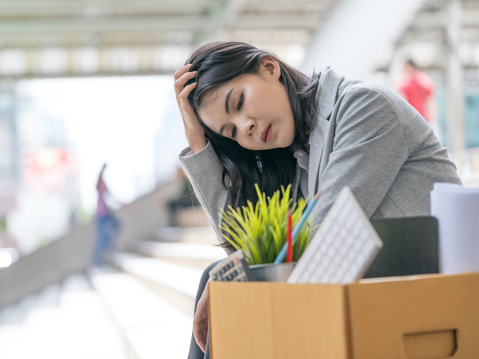 Businesswomen sitting on steps outside and has a box filled with office stuff next to her