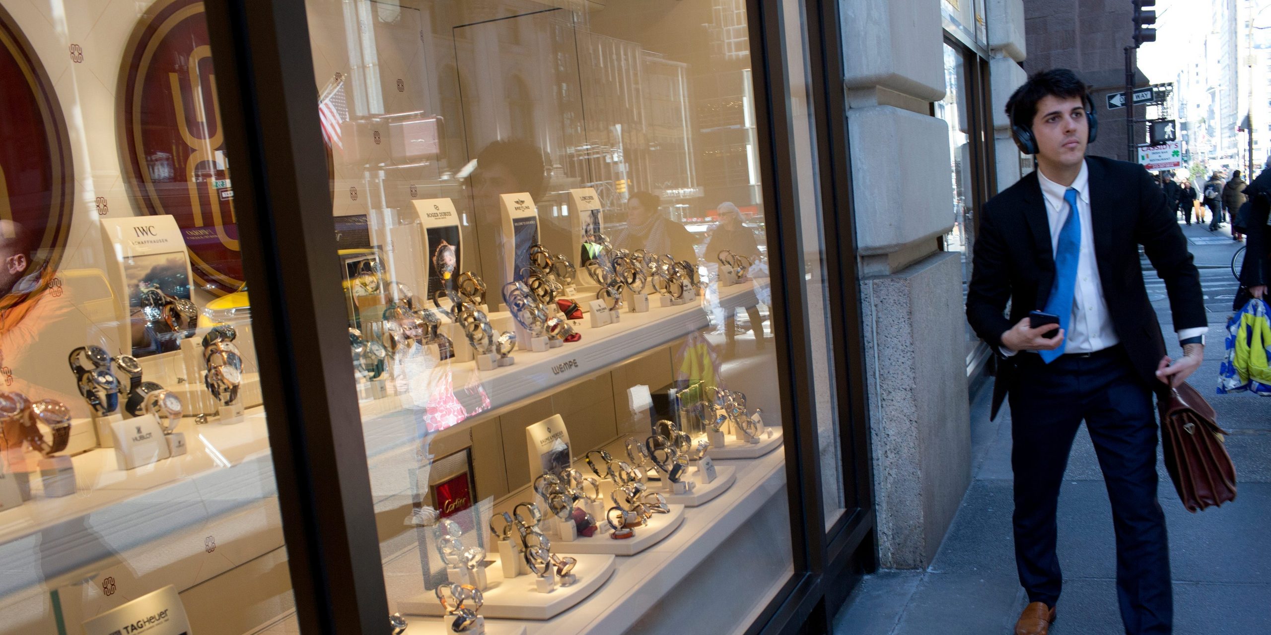 A young man in a suit walks past a luxury watch shop on 5th Avenue in New York City.