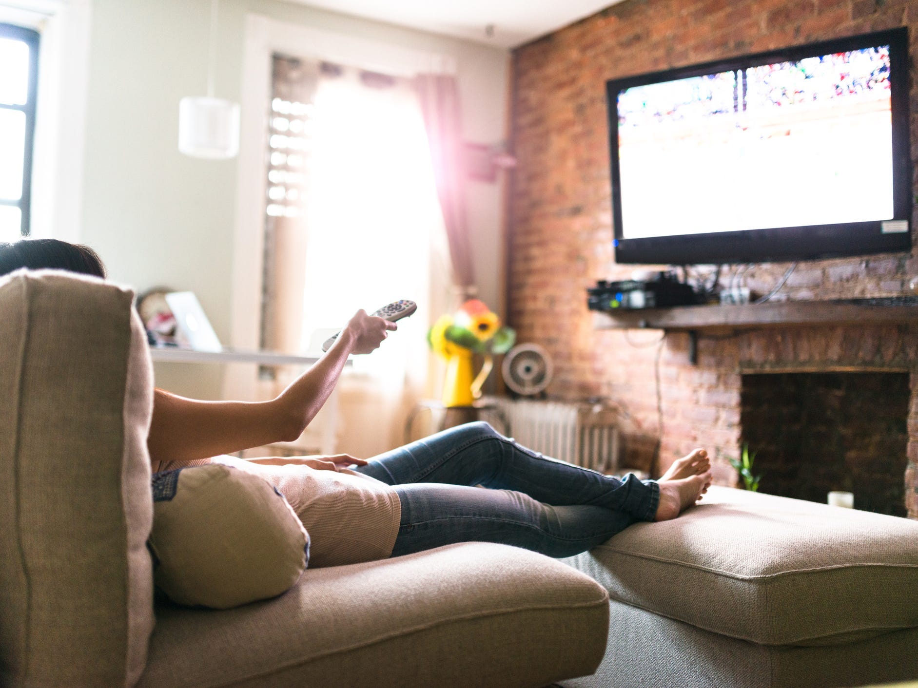 Person watching TV on the couch, using the remote to change channels