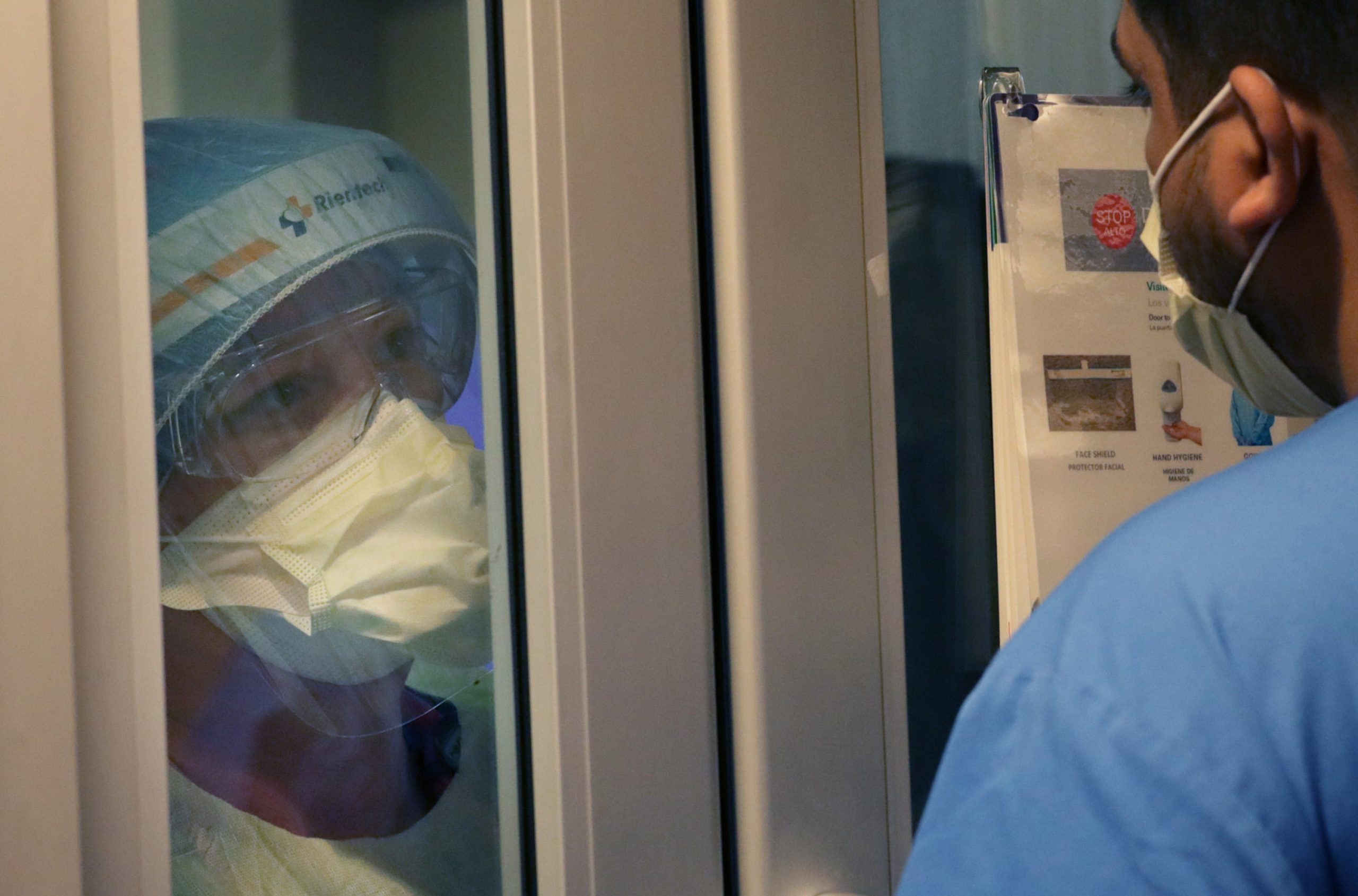 doctors in ppe look through hospital room door