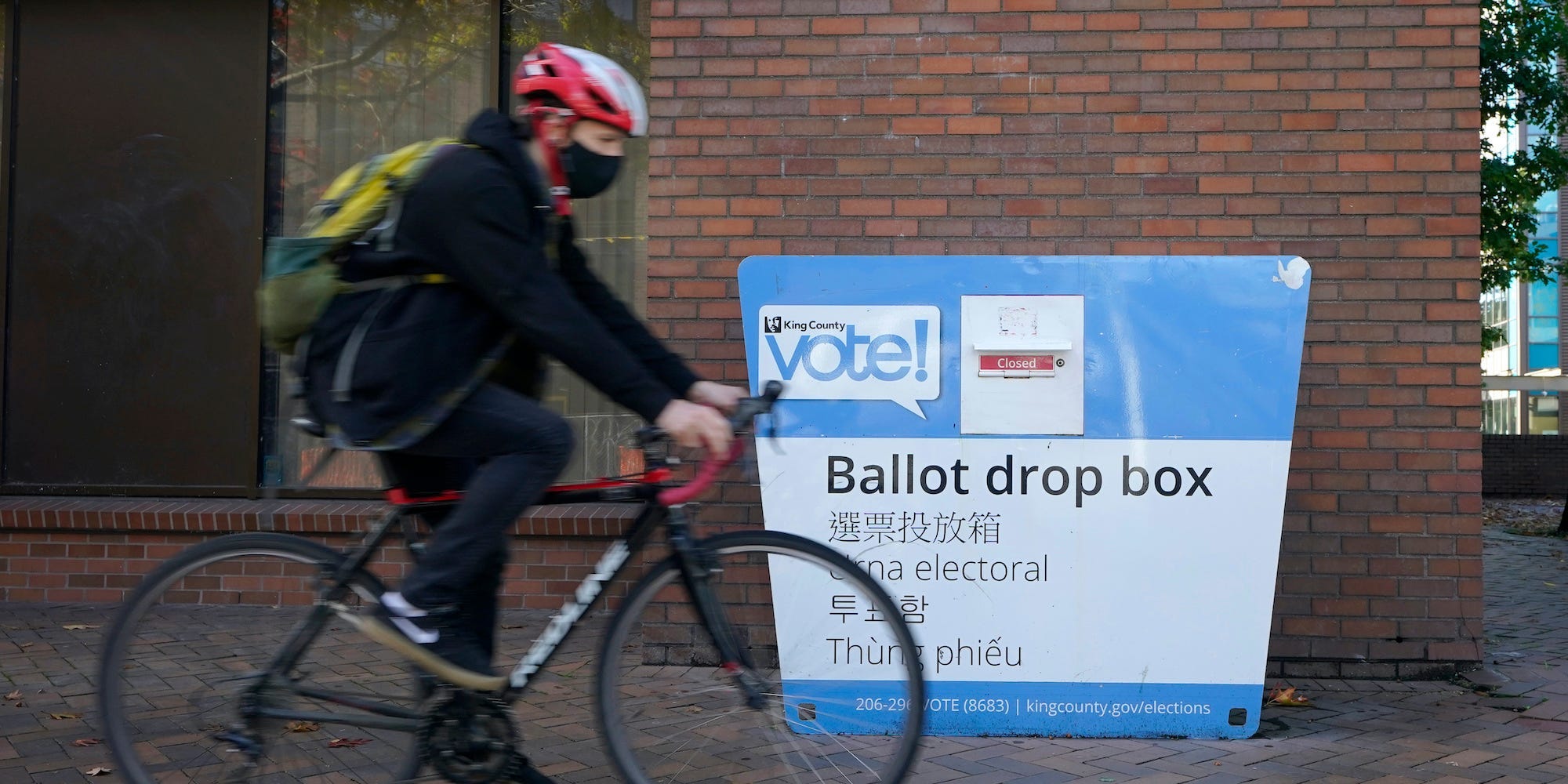 A cyclist rides past a ballot drop box, Tuesday, Oct. 13, 2020, in Seattle