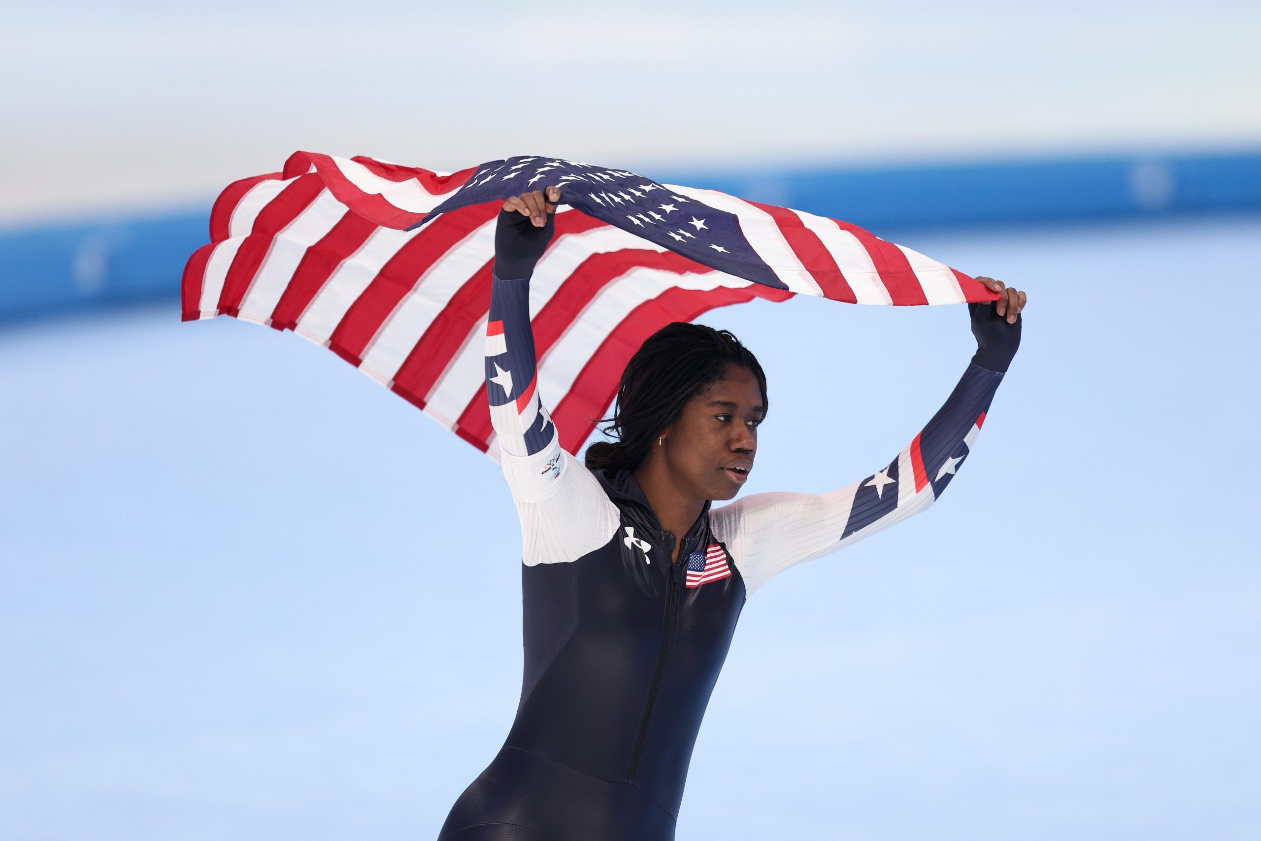 Speed skater Erin Jackson carrying American flag above her head after winning gold medal