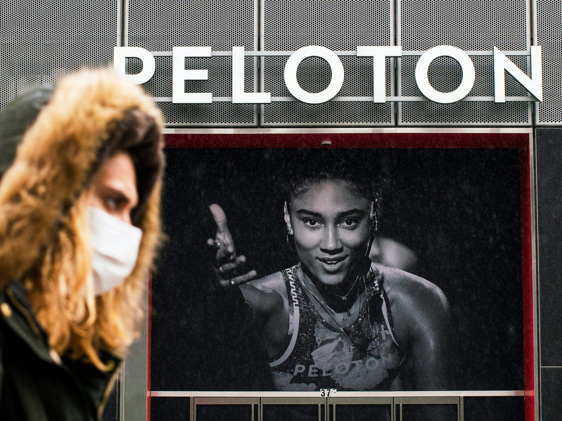 Woman walks in front of Peloton store with hood on and Peloton instructor poster large in background