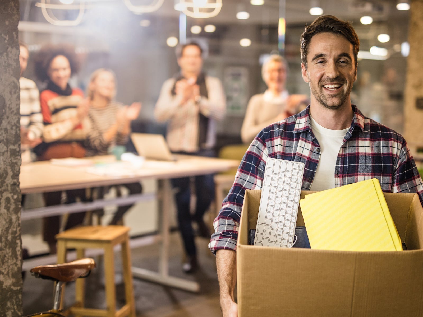 Male worker with a box of office stuff quitting his job. There are people in the background.