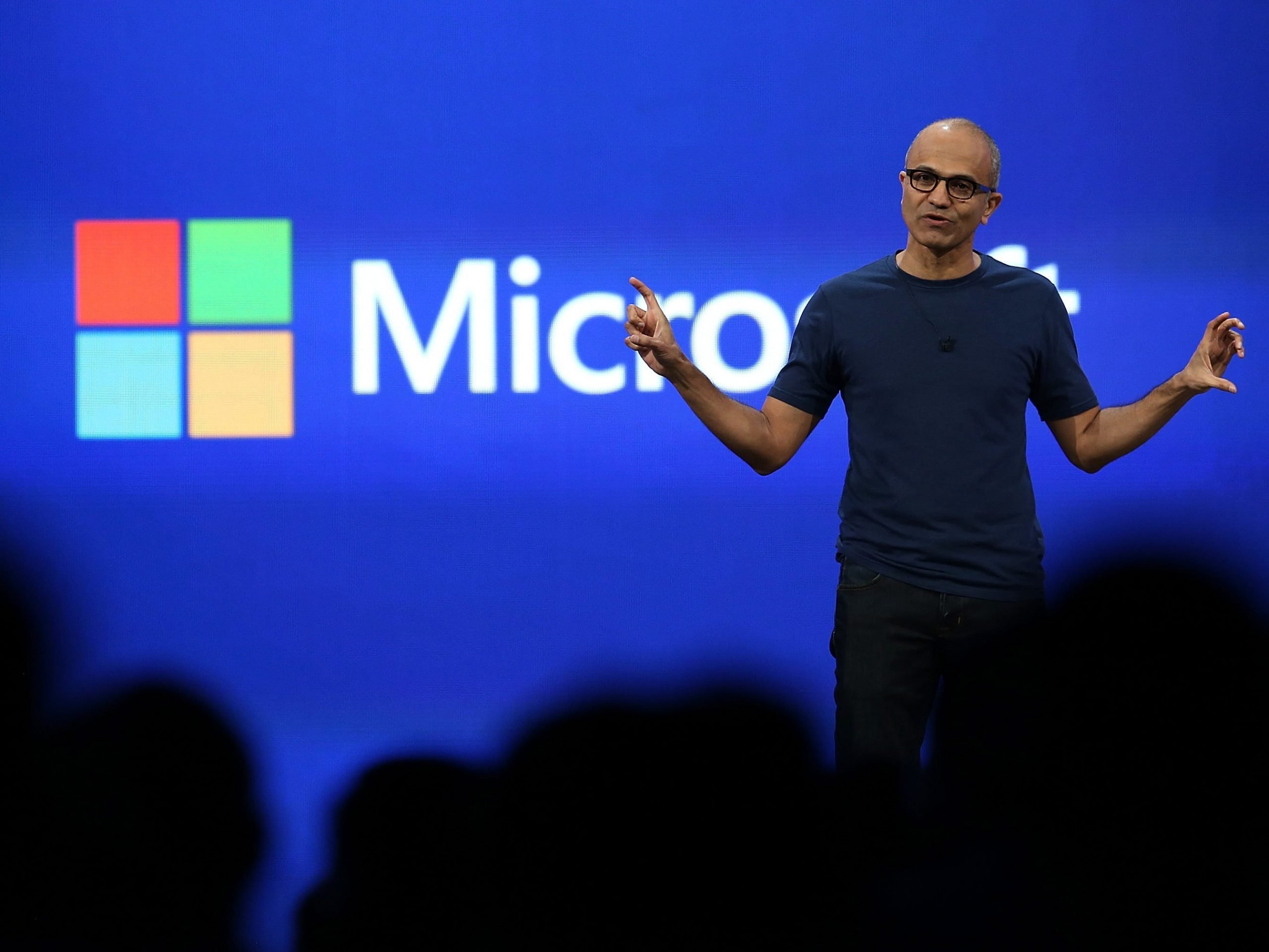 Microsoft CEO Satya Nadella stands on stage and gestures widely with both hands