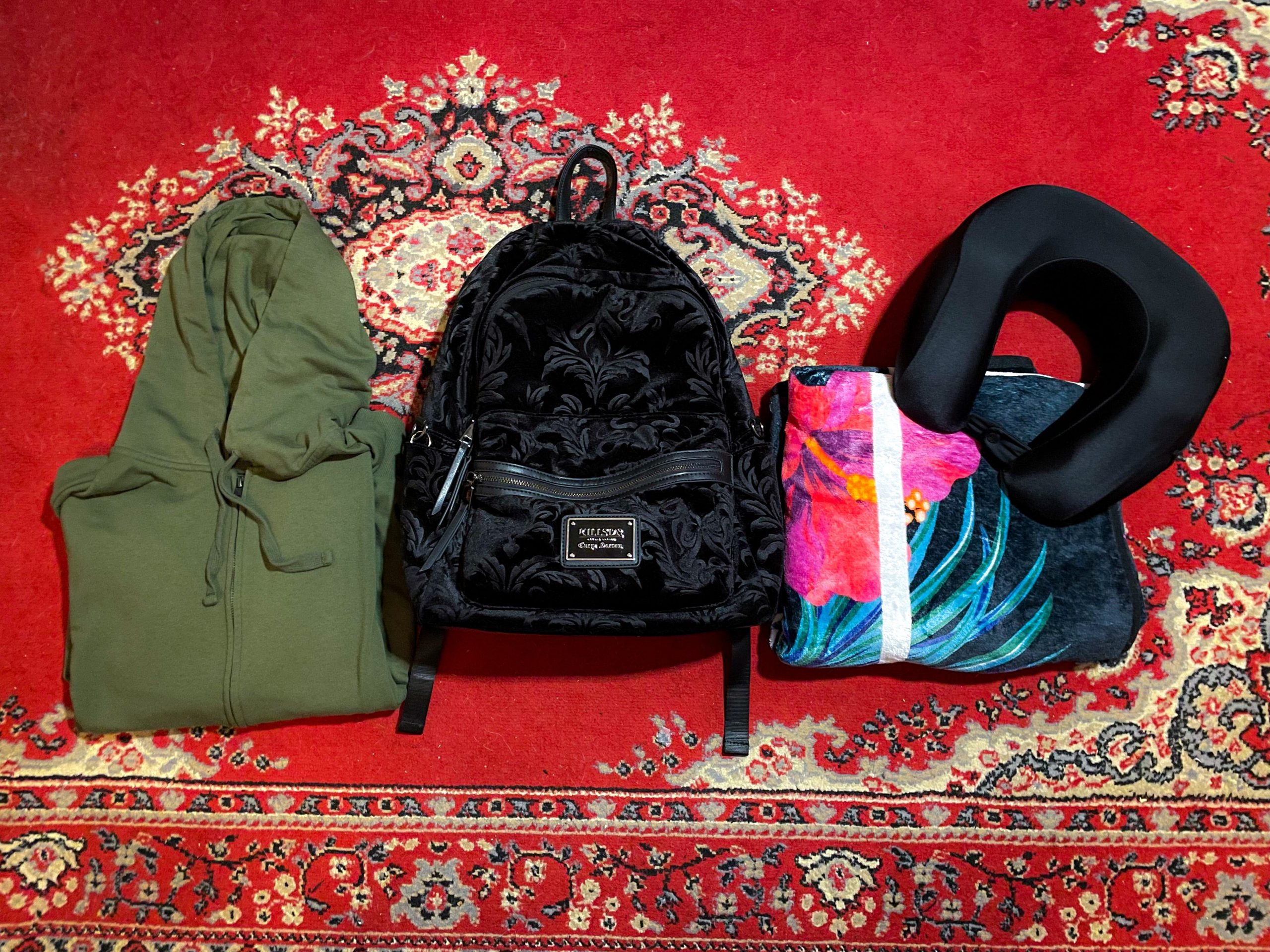 Backpack, zip-up hoodie, blanket, and neck pillow on a carpet