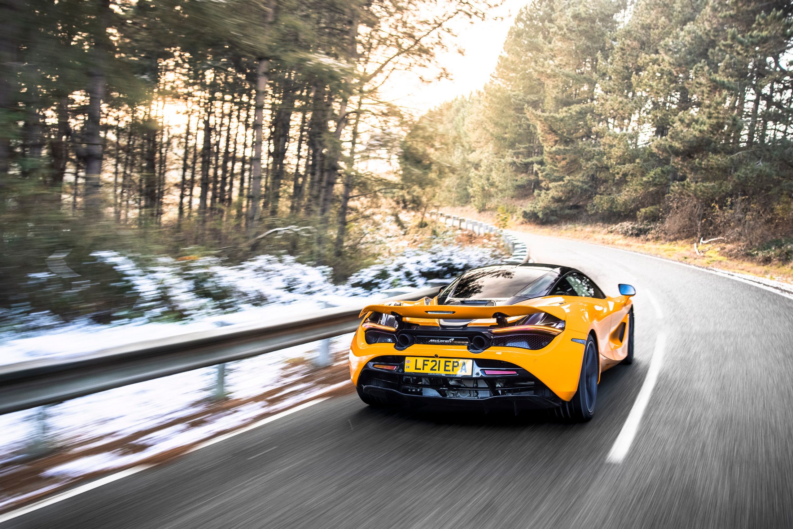 An orange McLaren 720S on a wooded road.