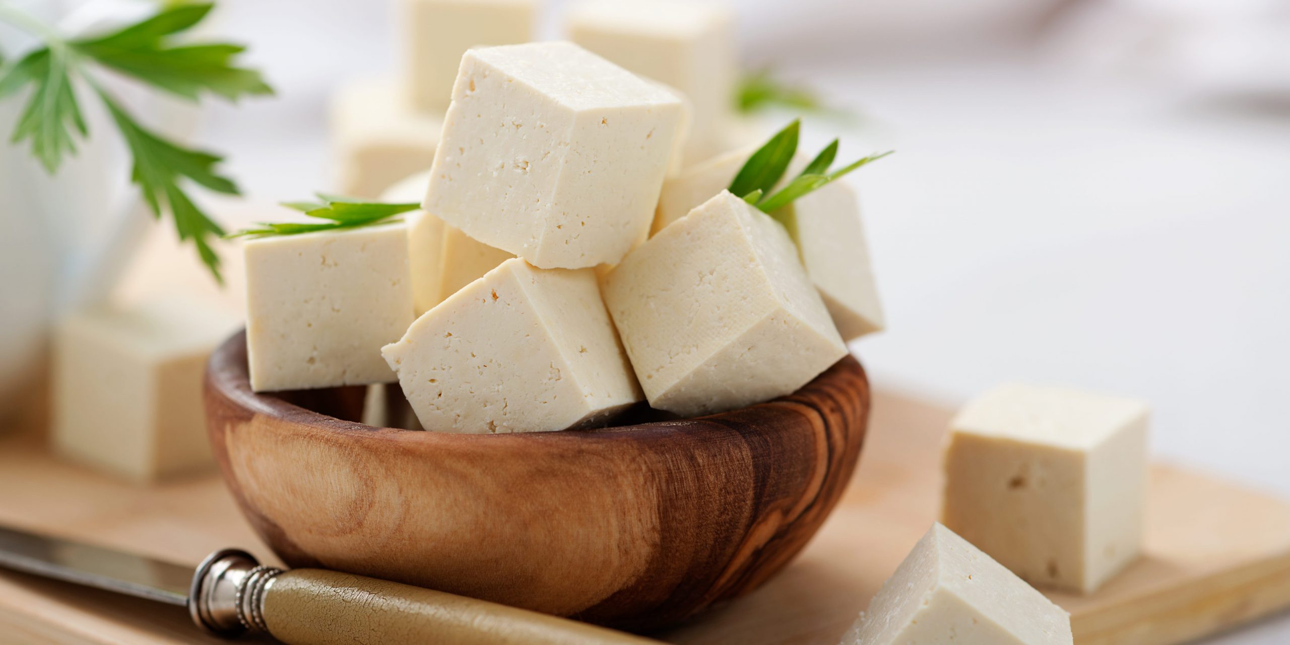 Cubed tofu in a bowl on a cutting board with a white background