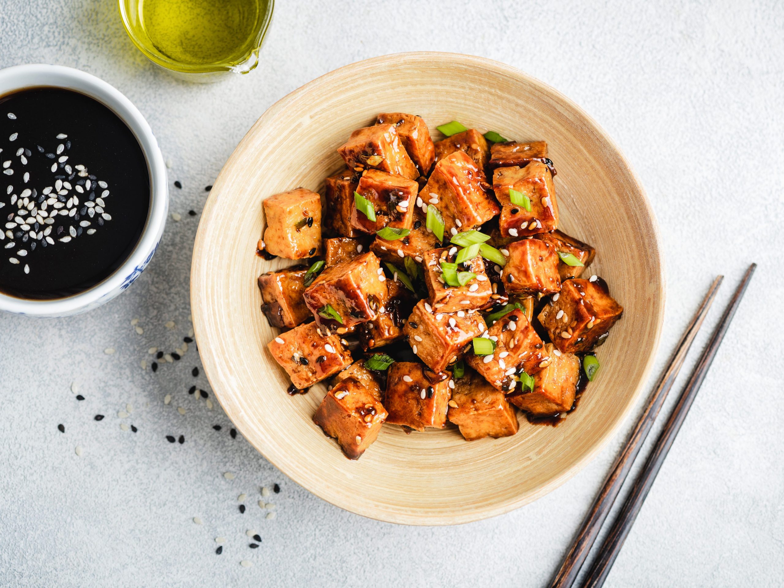 Fried tofu tossed in an East-Asian inspired sauce topped with scallions in a bowl