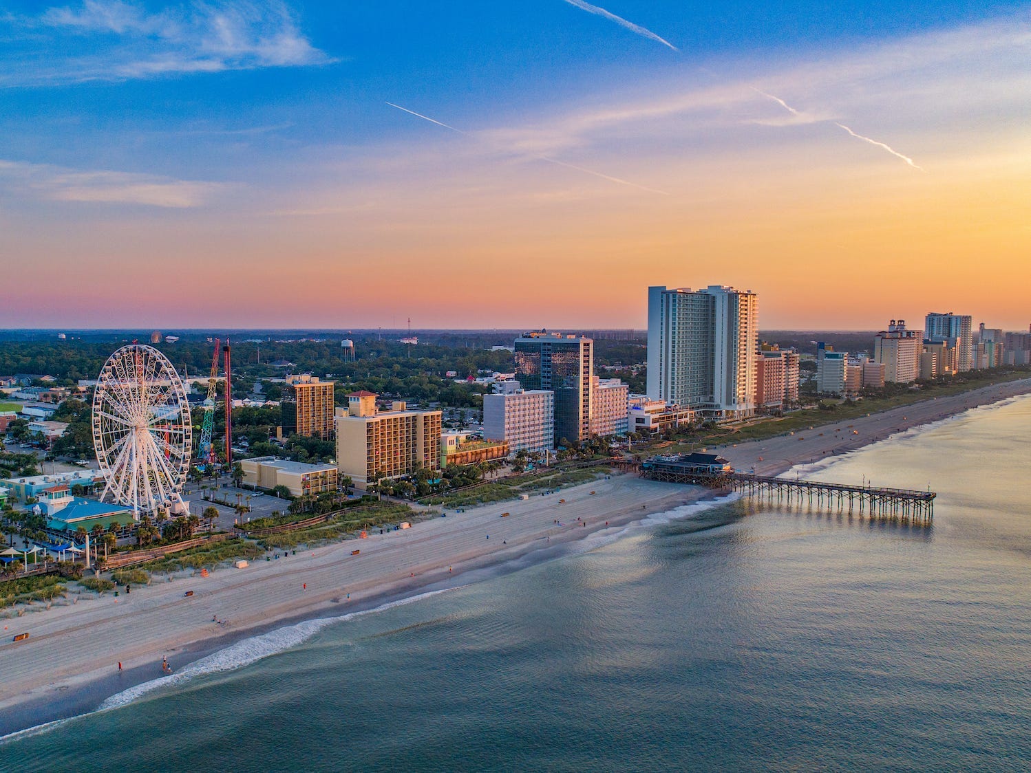 The shore of Myrtle Beach, South Carolina, with a long beach, a pier, and a Ferris wheel.