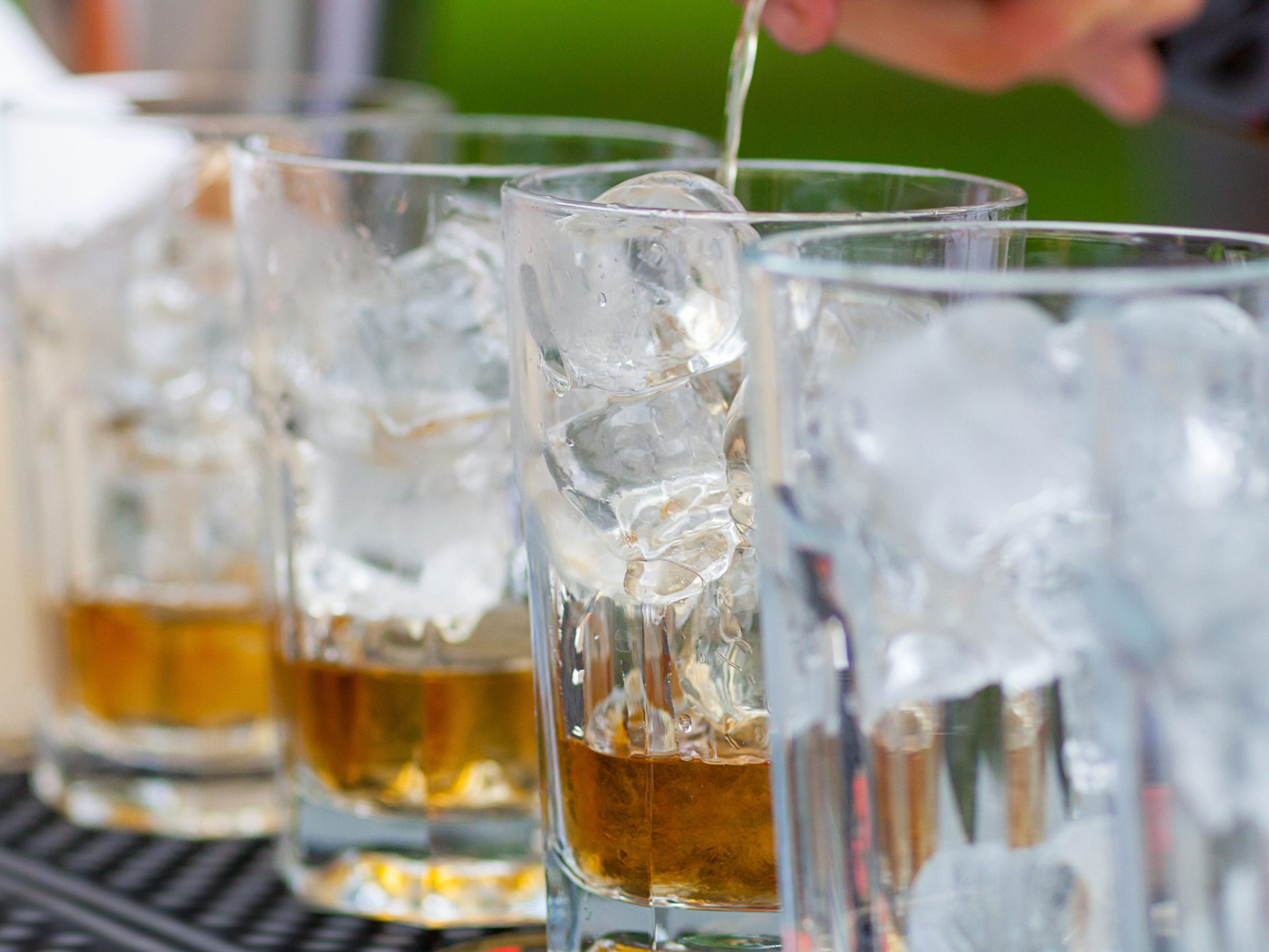 hand pouring liquor into glasses with ice at an outdoor bar for an event wedding