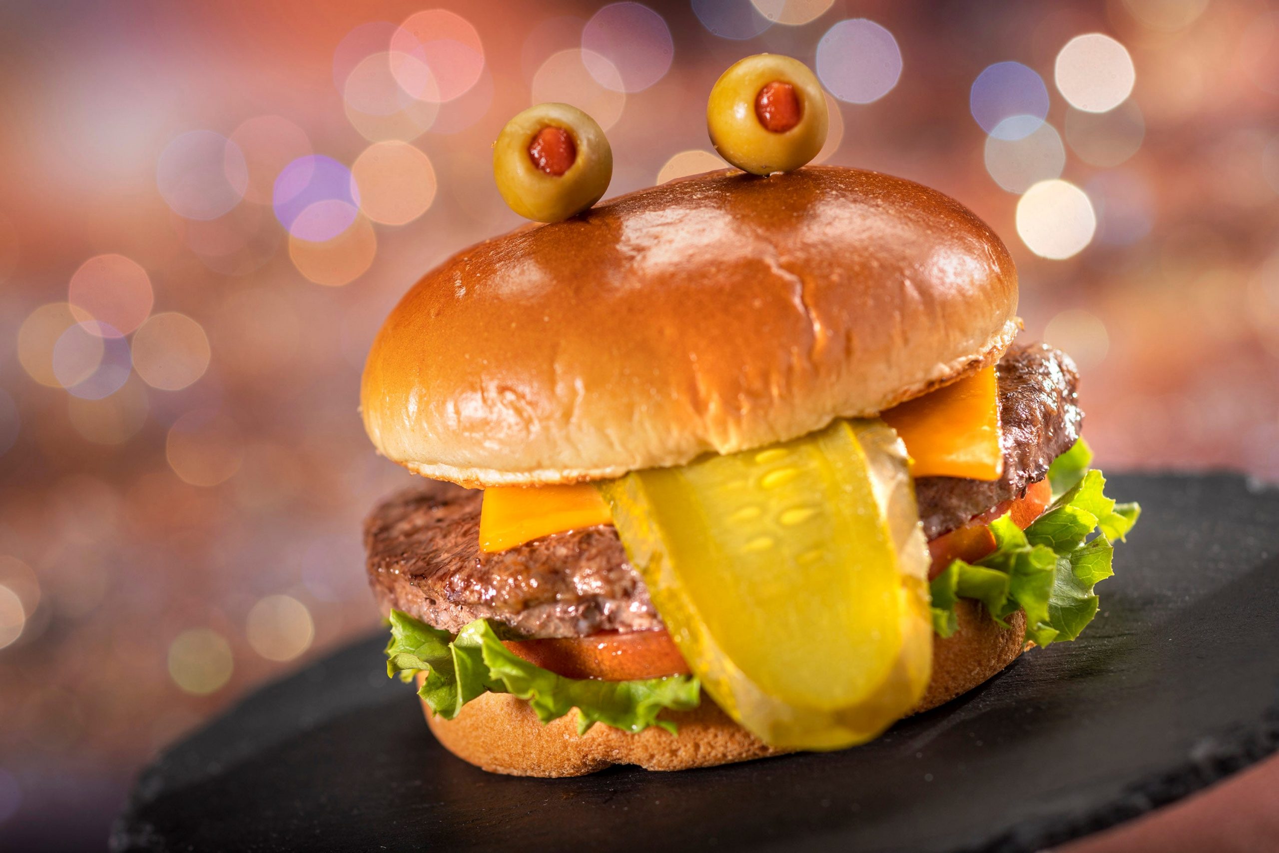 A hamburger with a pickle slice acting as a tongue and two olives on top of the bun, meant to resemble eyes.