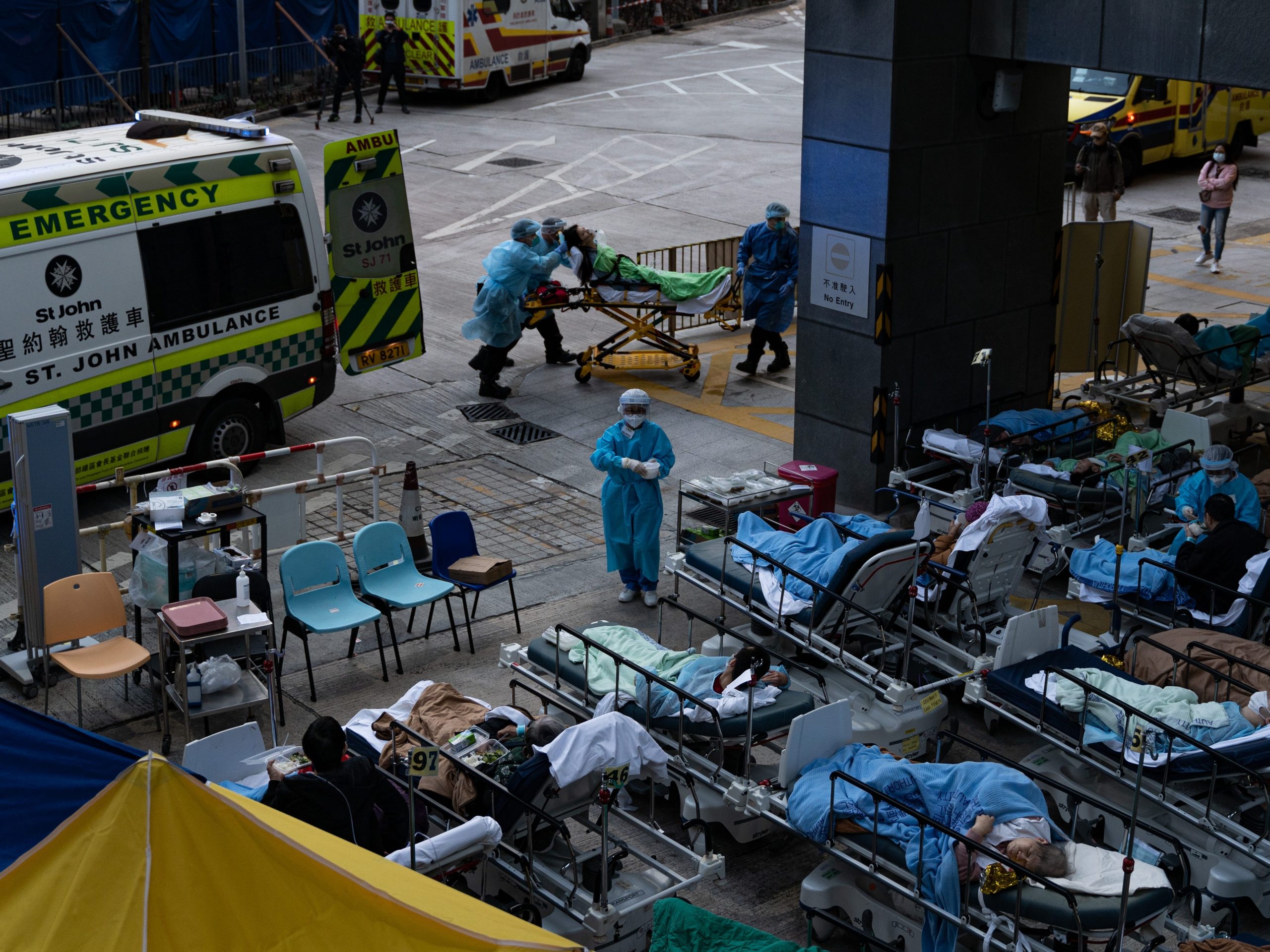 On February 16, 2022, a patient lies in a hospital bed waiting for medical treatment in a temporary holding area outside Caritas Medical Center in Hong Kong, China, as medical staff take out a new patient from an ambulance.