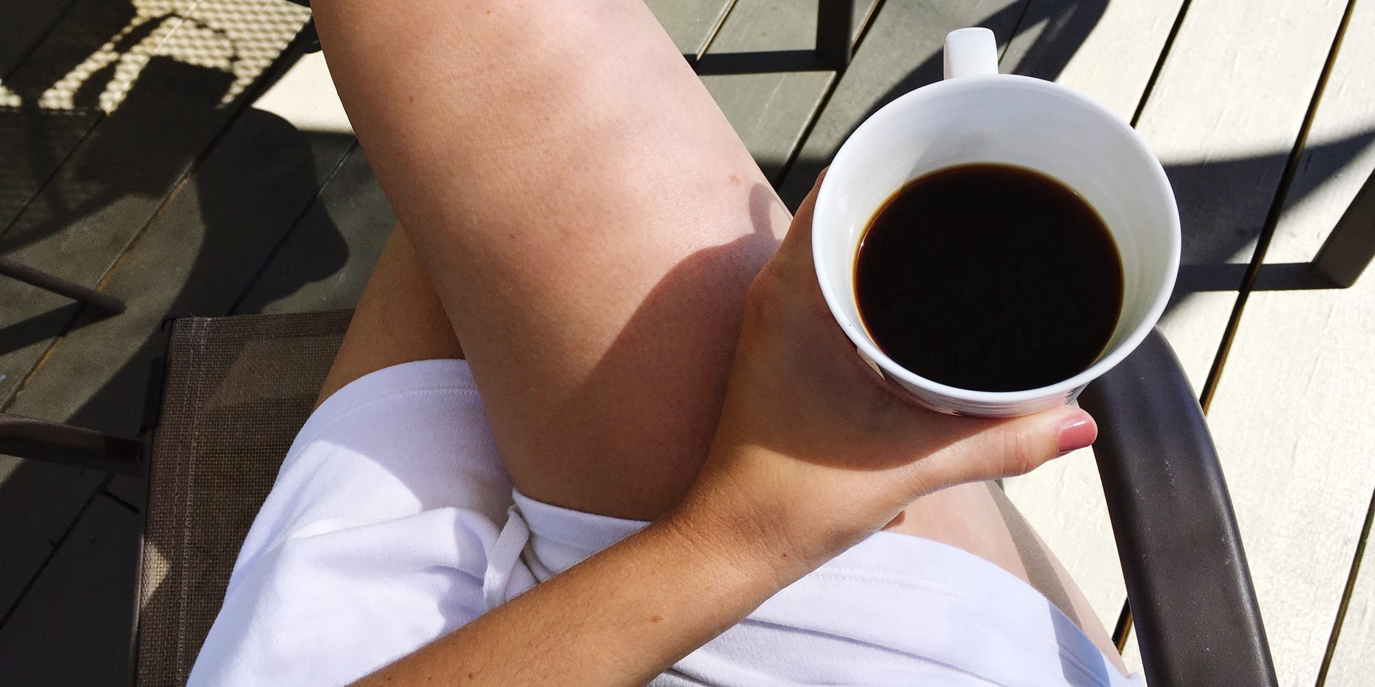 A person sits with their legs crossed holding a cup of coffee.