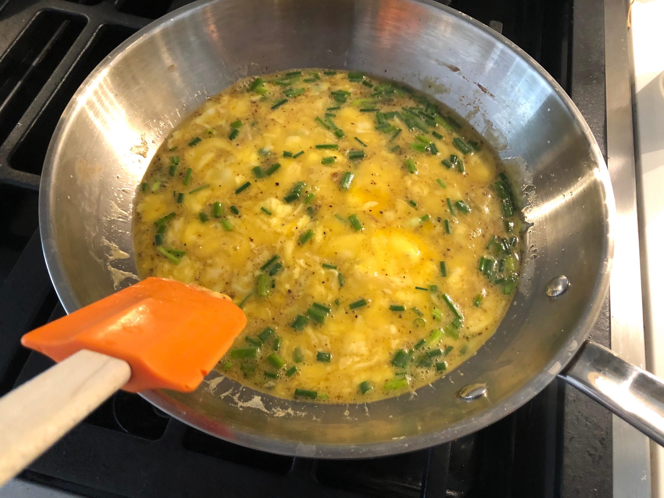 Eggs being scrambled with chives in a pan with rubber spatula