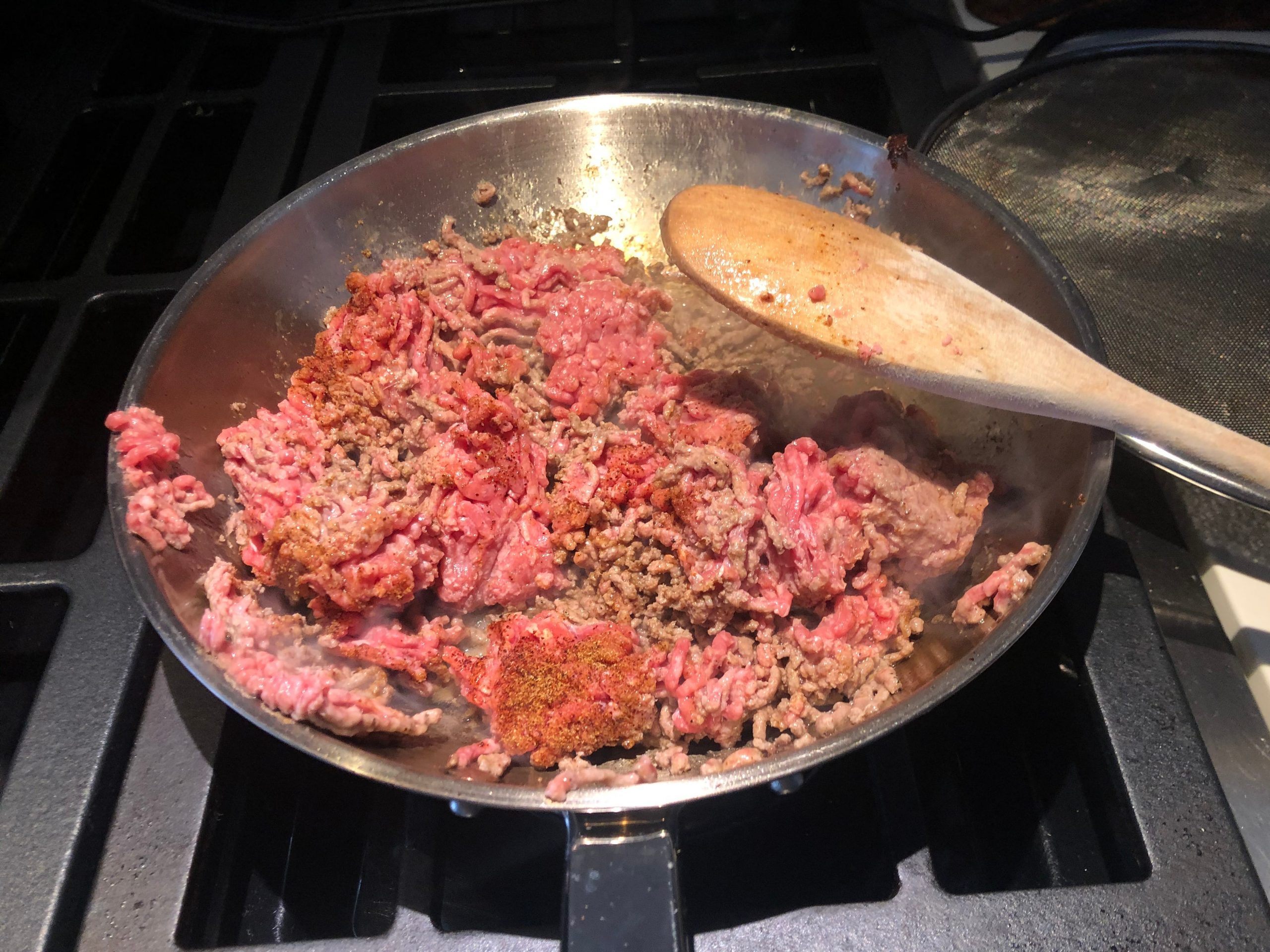 Cooking beef in pan on stove with wooden spoon