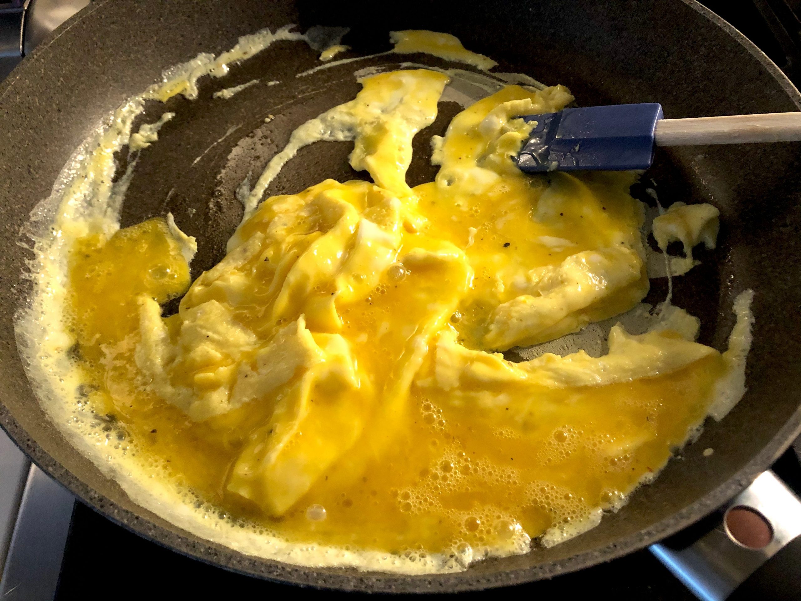 Eggs being scrambled in pan with rubber spatula