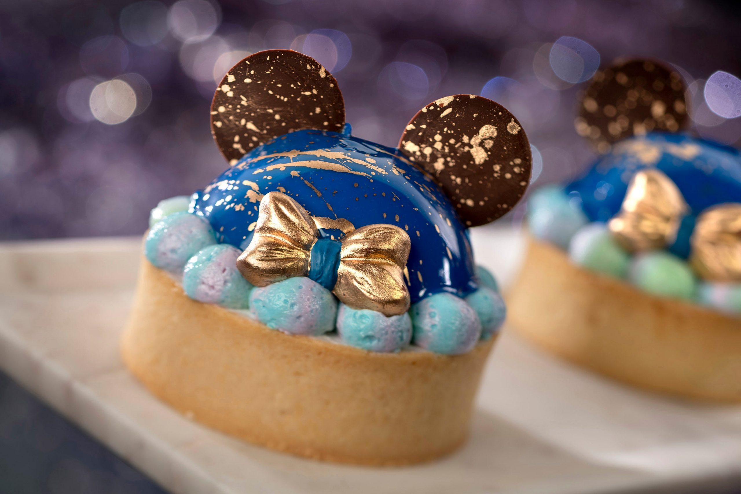 One of Disney's culinary creations, which is a small sponge cake with a blue and gold mouse head outline on top.