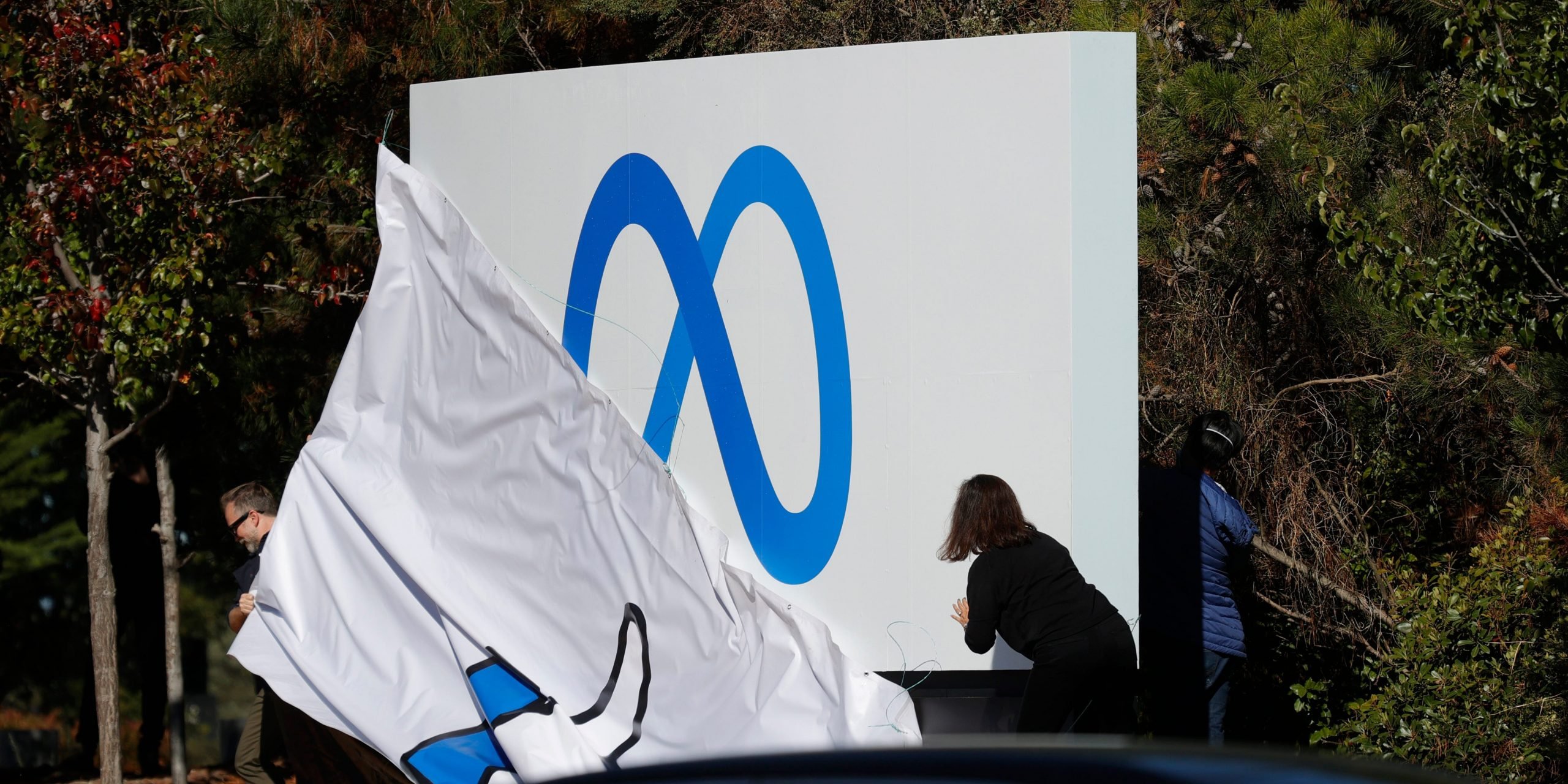 Workers in front of Facebook headquarters pull off cover of the old "thumbs up" sign to reveal the new Meta logo