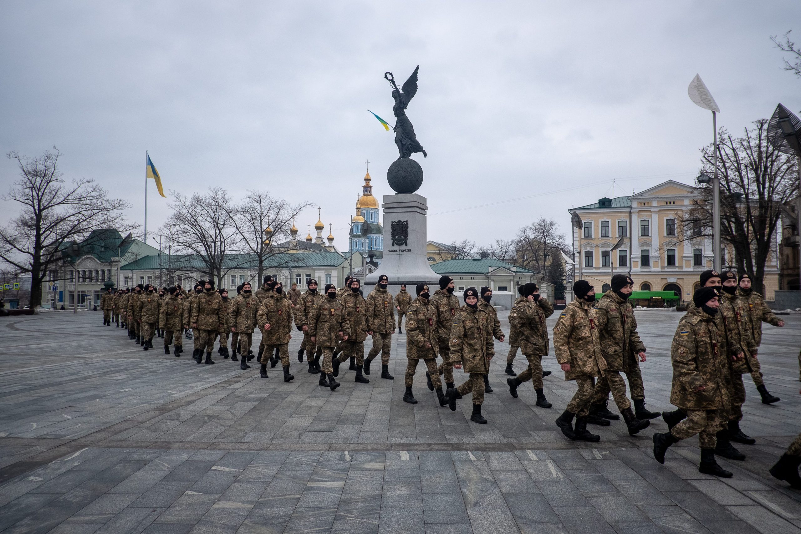 Ukrainian military cadets walk through a Ukrainian city, with a monument and a church seen in the background.