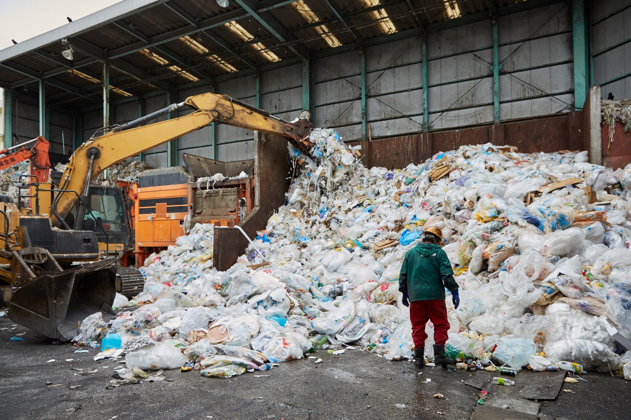 A worker stands in front of a pile of plastic waste as machinery processes it at a facility in Japan.