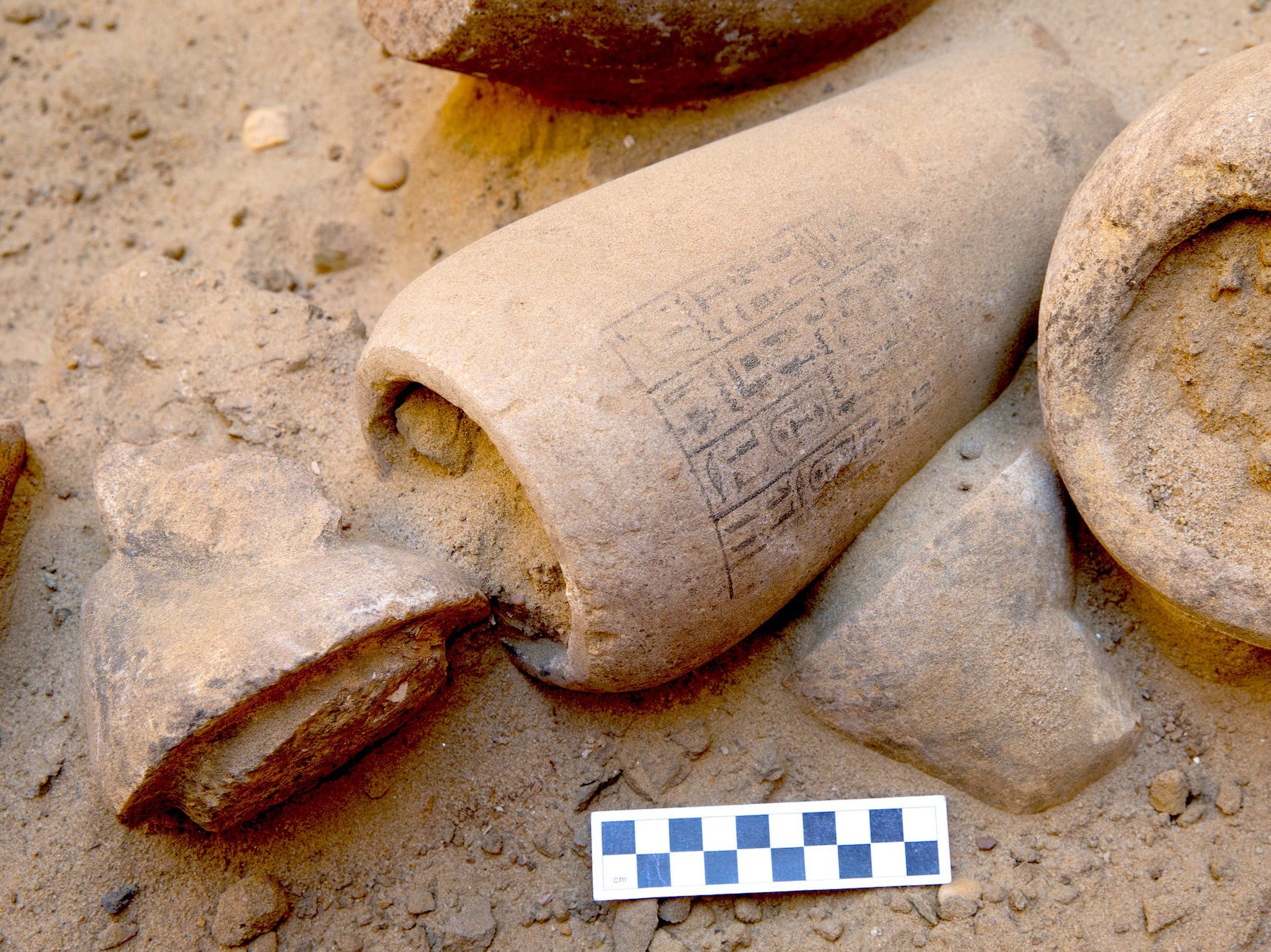 A jar is shown as found at the Abusir site, opened, with the lid having some sort of animal head on it and the body being covered with hieroglyphics.