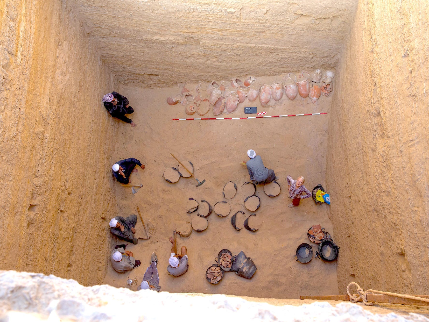 The embalming shaft is seen from the surface, with people excavating the site at the bottom of the shaft.