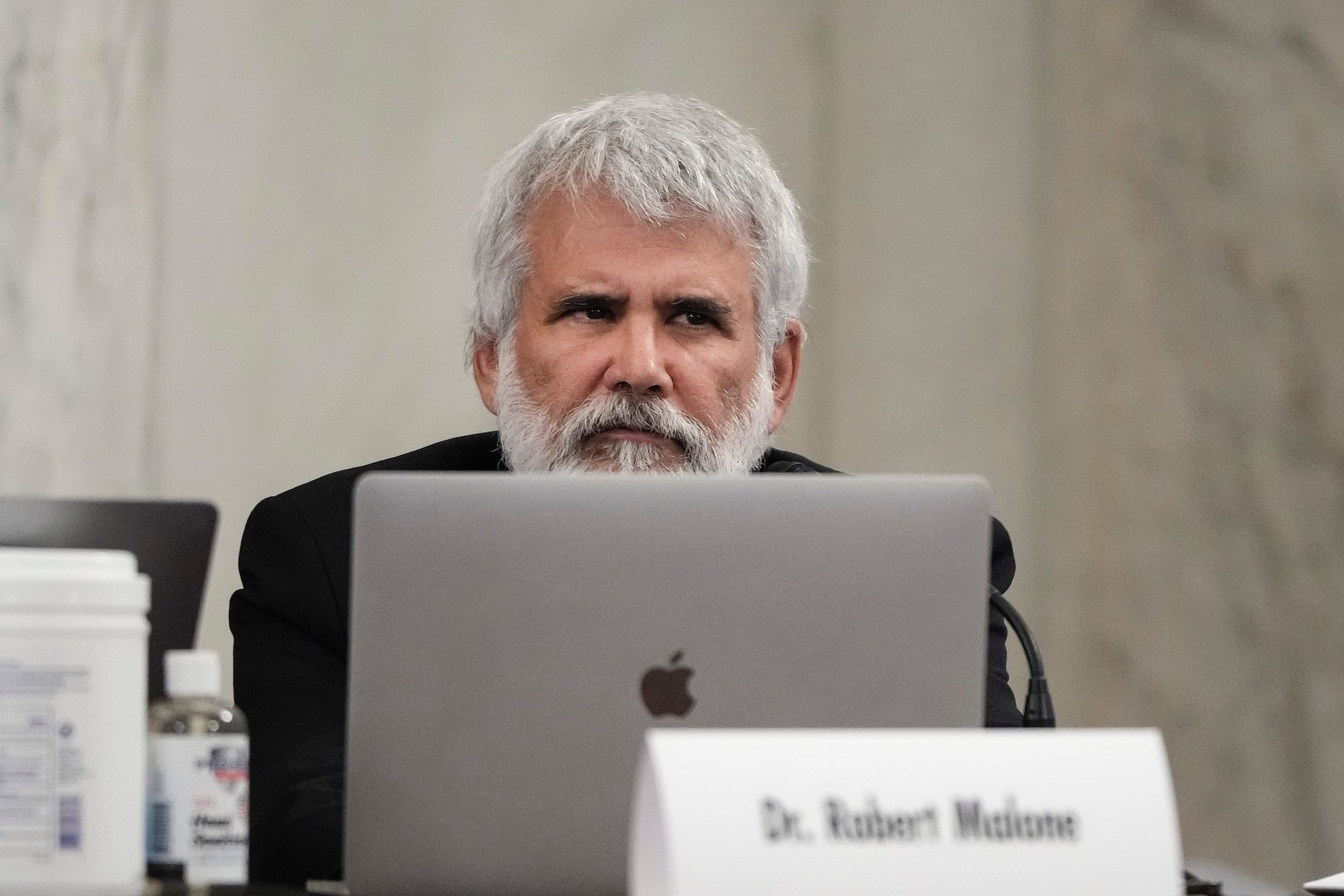 robert malone on capitol hill, sitting in a suit, with laptop