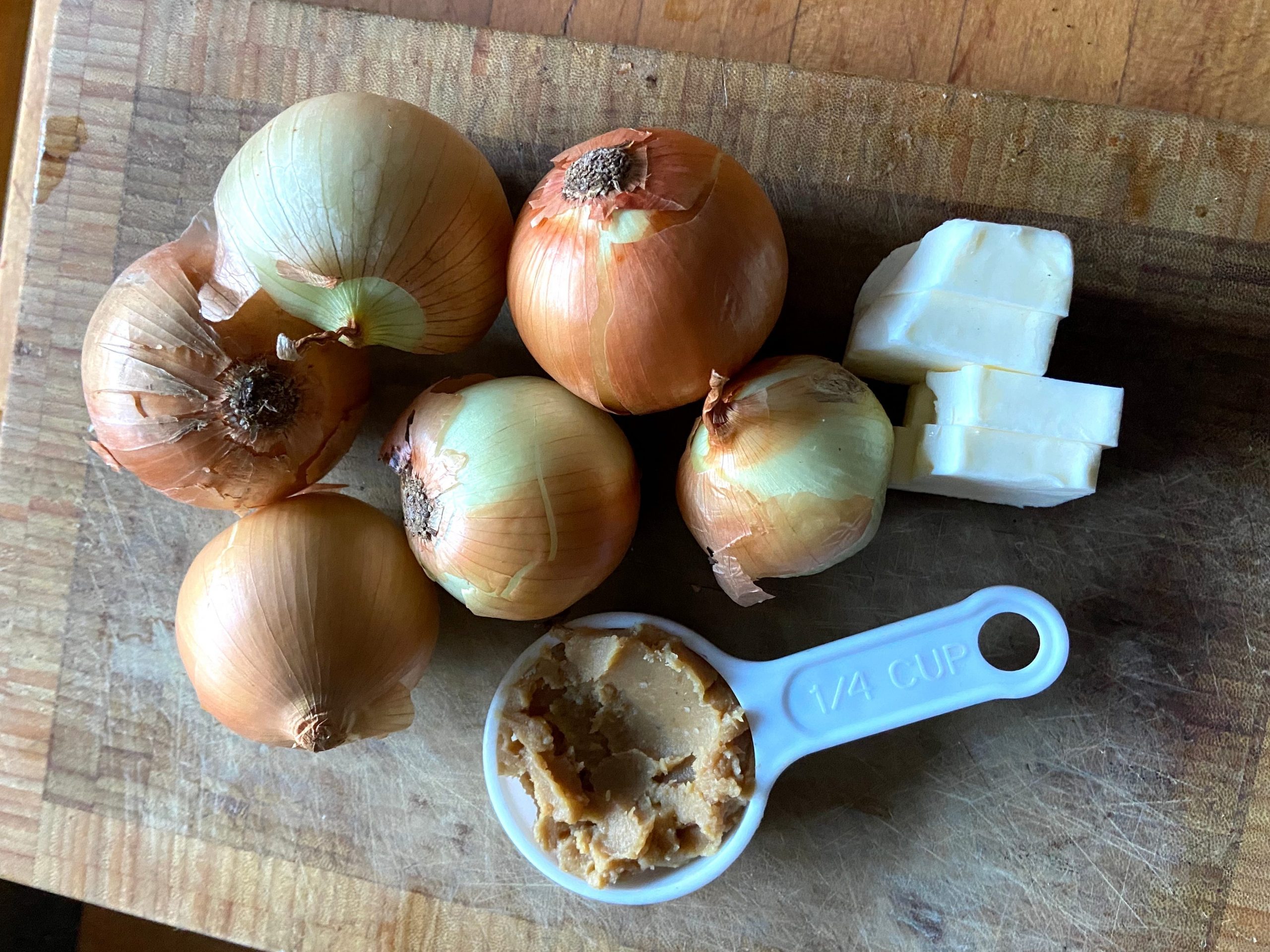 Yellow onions, miso paste, and butter on a wood cutting board