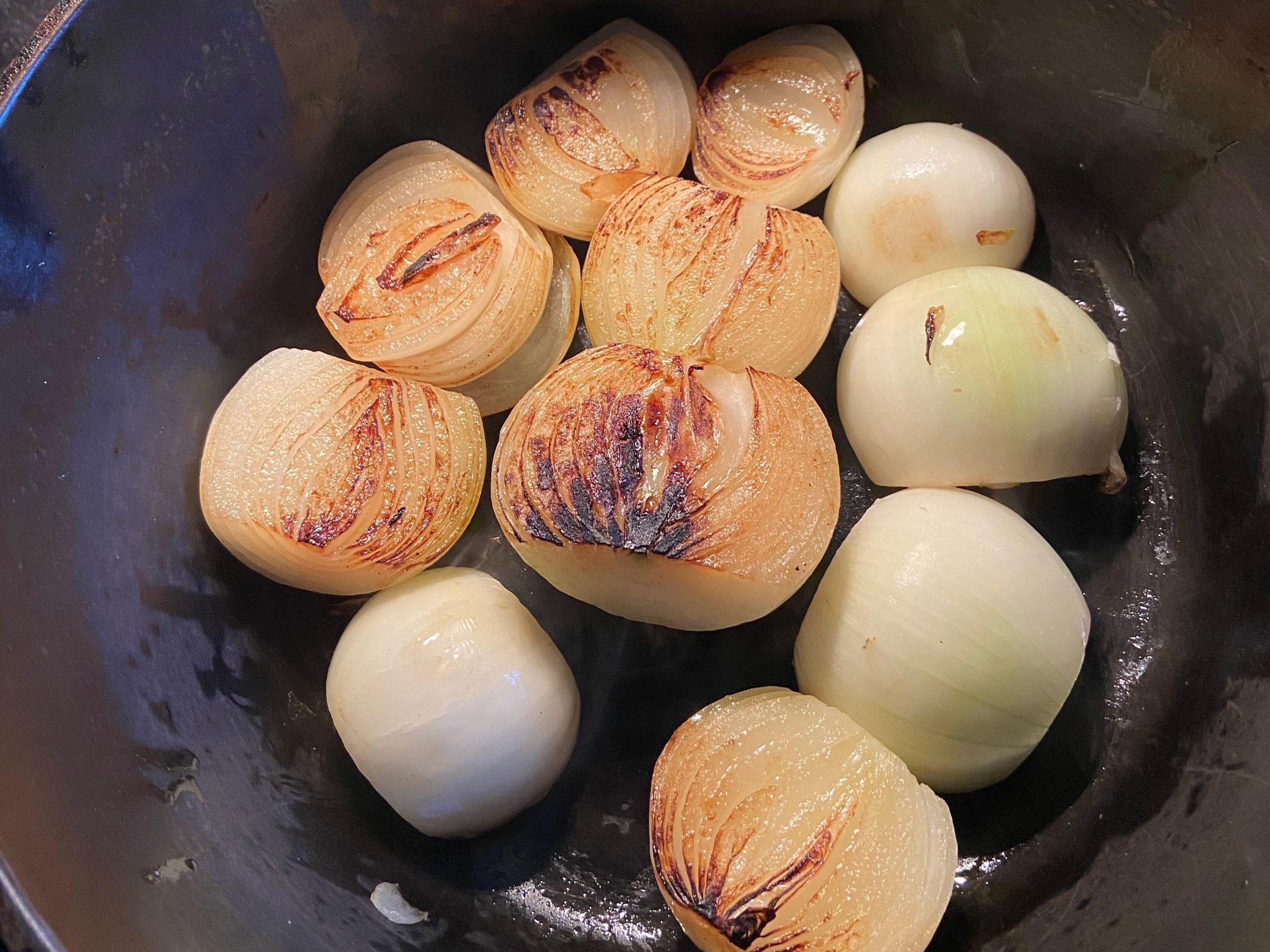 Halved Yellow onions cooking in a deep pan on stove