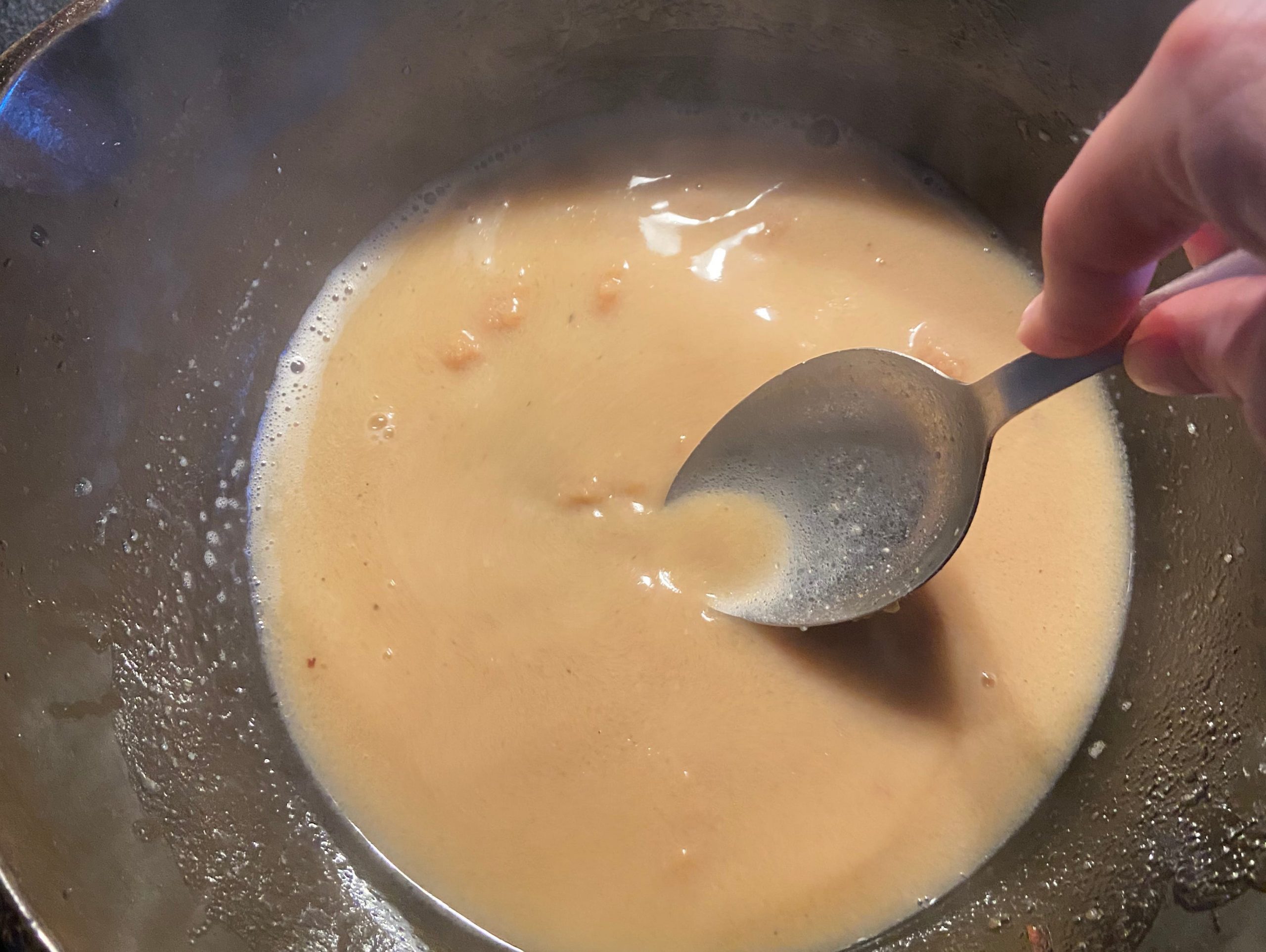 Miso and butter broth cooked in a deep pan over the stove being stirred with spoon