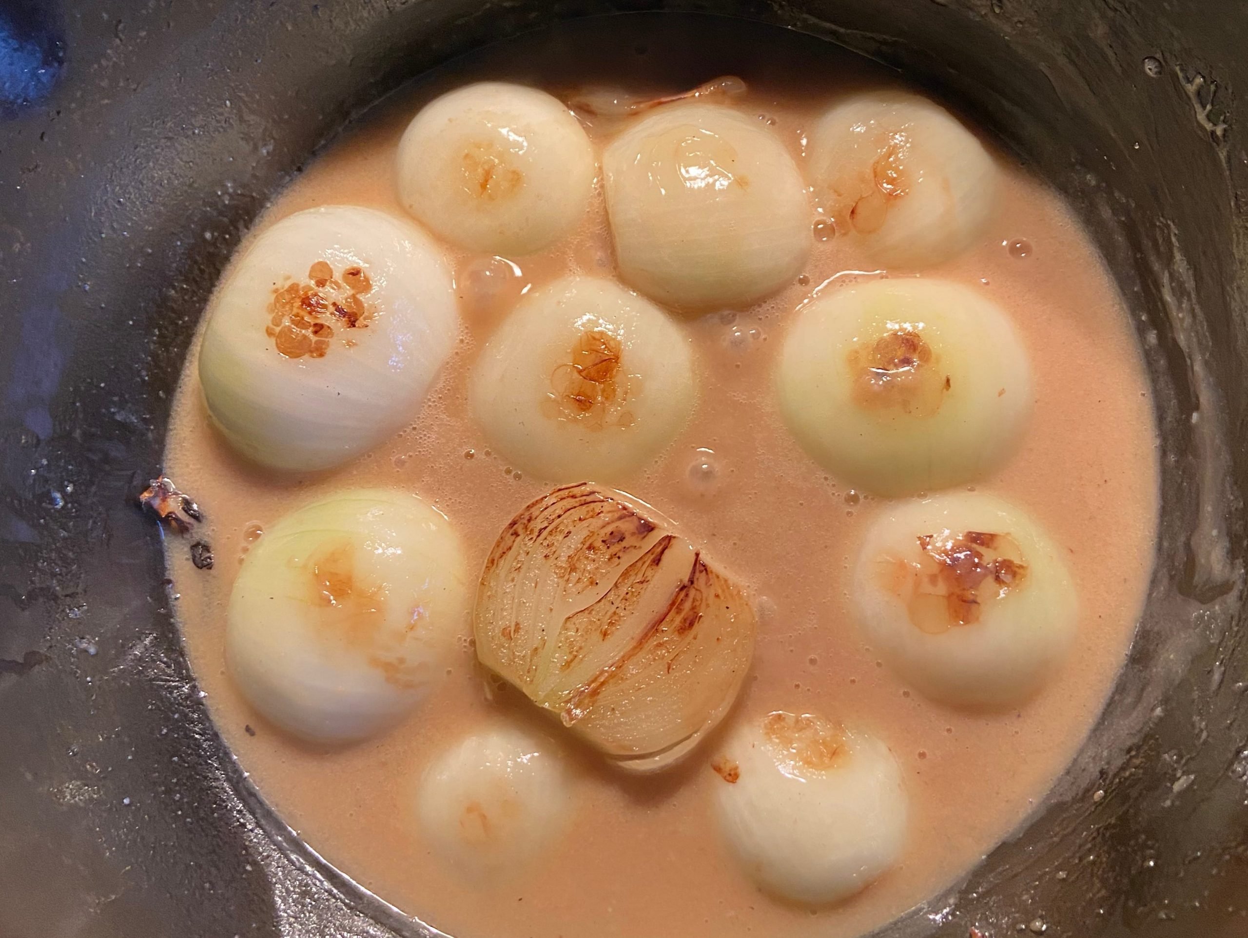 Halved yellow onions braising in miso-butter broth in pan over stove