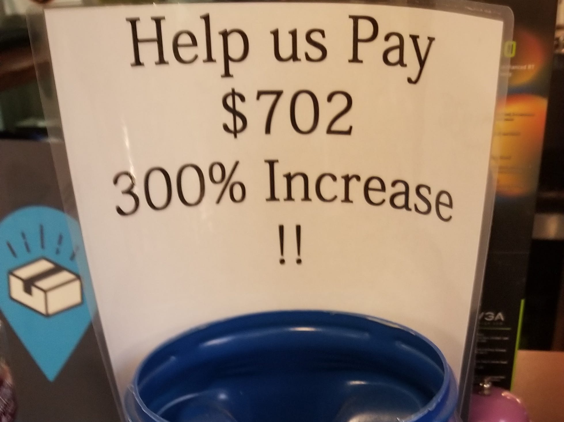 A blue plastic jar with Con Edison's logo on it, with a sign taped to it that says "Help us Pay $702 300% Increase!!"