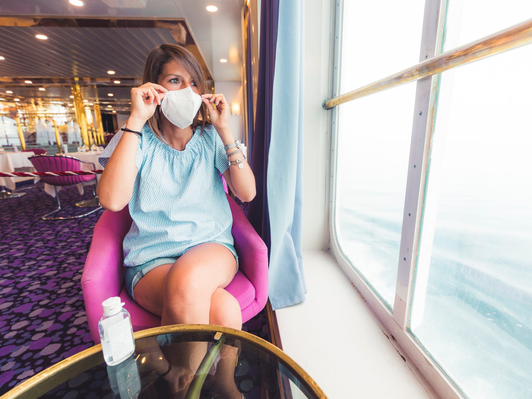 A person wearing a face mask while staring out a window on a cruise ship in Italy.