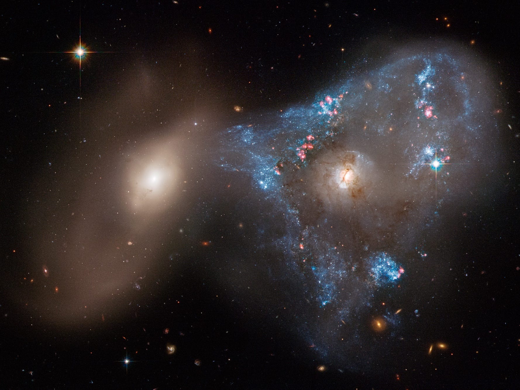 two galaxies merging one yellow one blue and pink