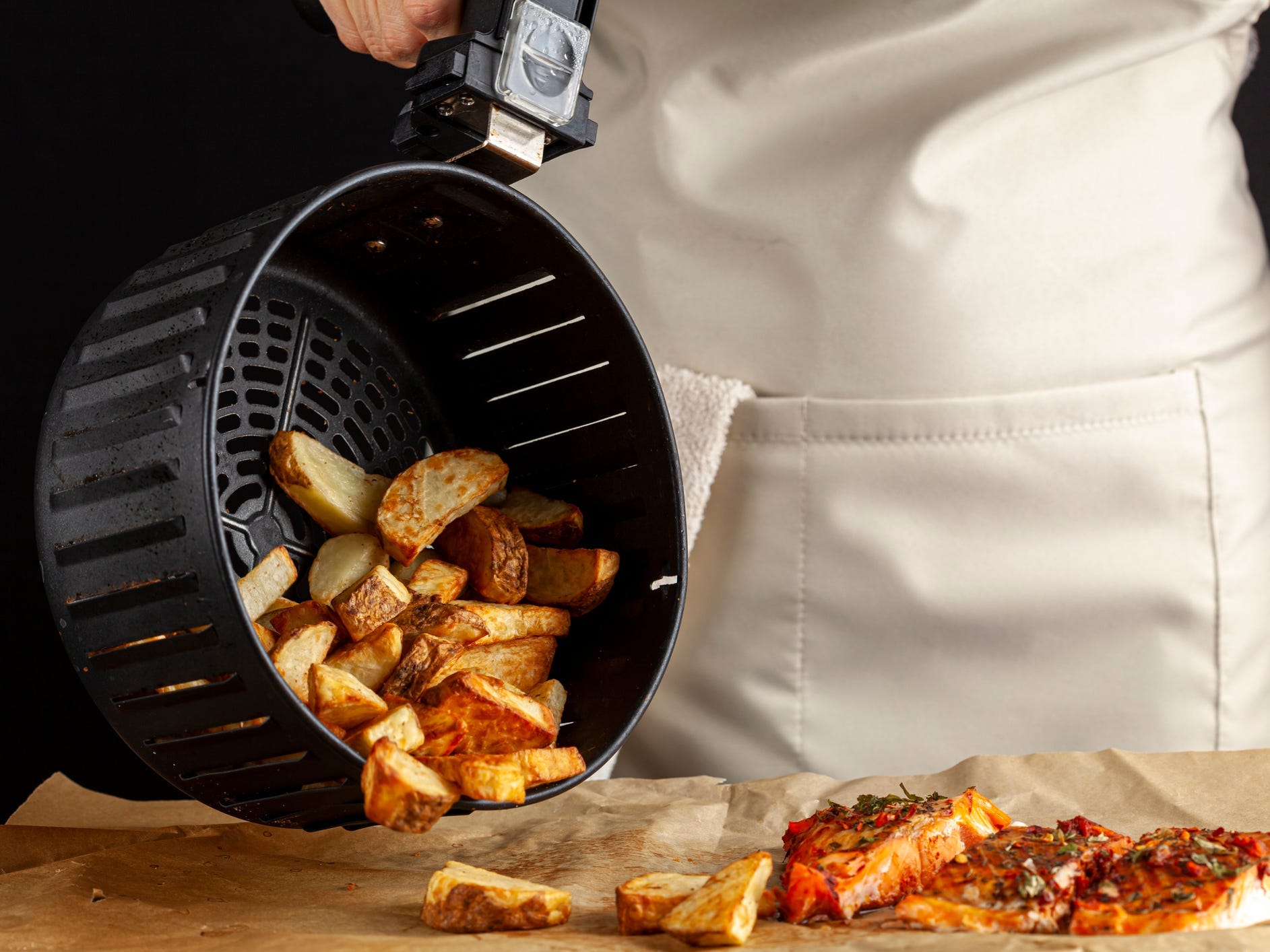 Person pouring air fried potatoes onto parchment next to cooked fish