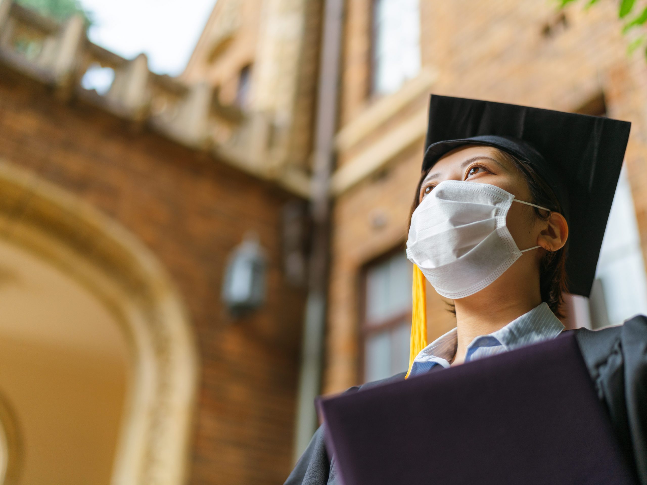 A low angle portrait of a student in graduate gown with a diploma.