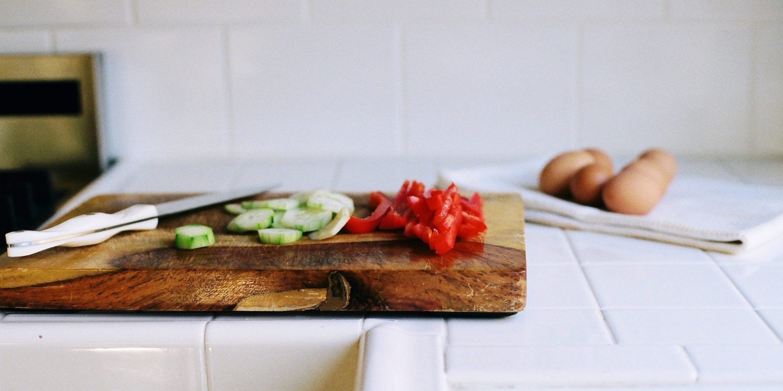 Frontal view of a wood cutting board with vegetables on top and some background styling