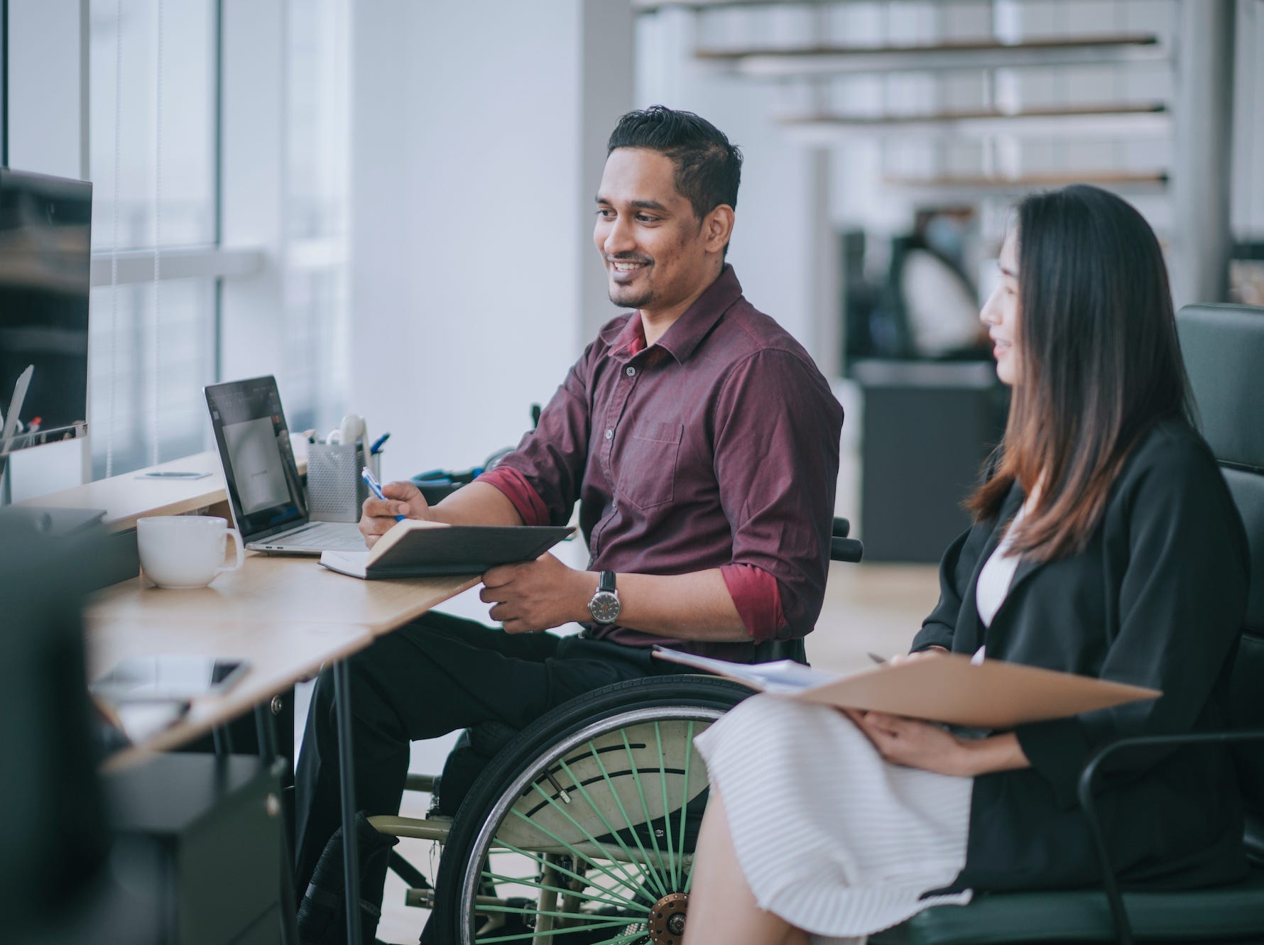 A worker in a wheelchair talking to a colleague in an office